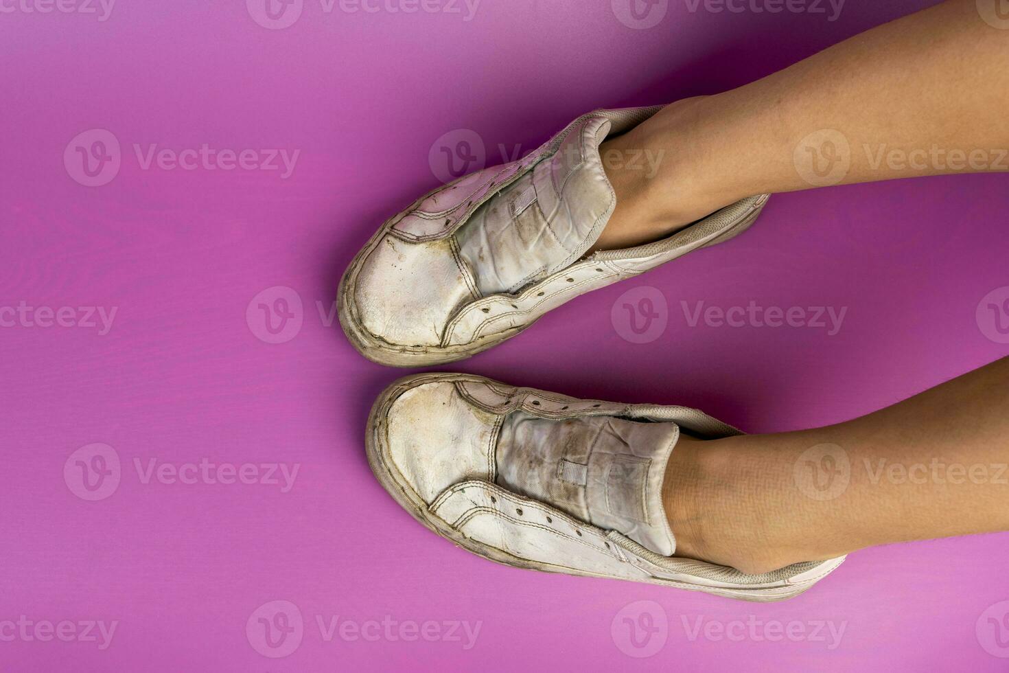 women's legs shod in old battered sneakers on a pink background photo