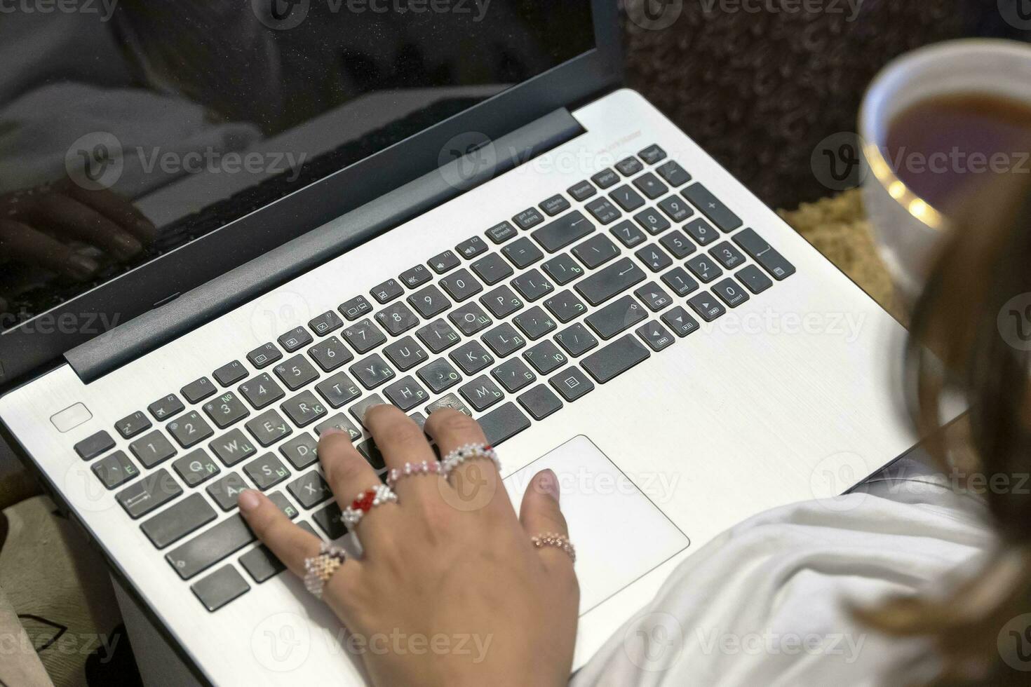 girl with a cup of tea in her hand is typing on a laptop photo