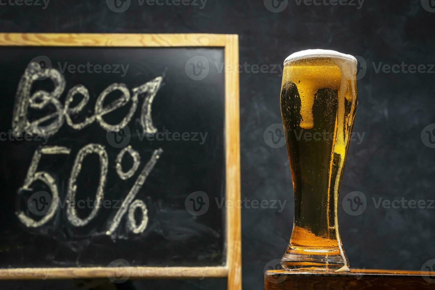 A glass of fresh and cold beer on a wooden table on a dark background. photo