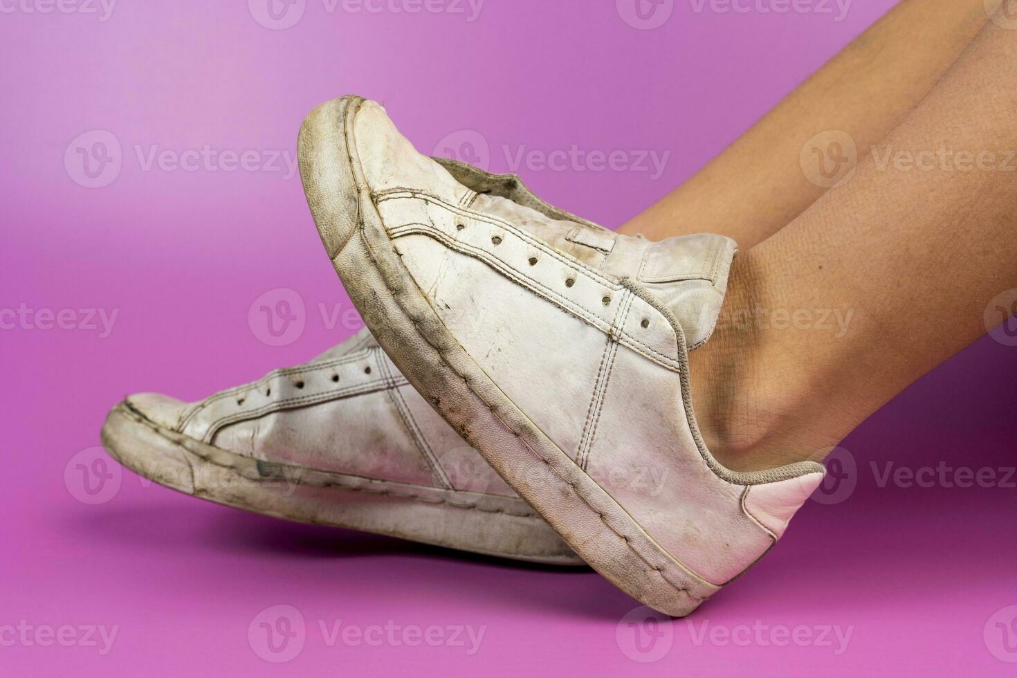 women's legs shod in old battered sneakers on a pink background photo