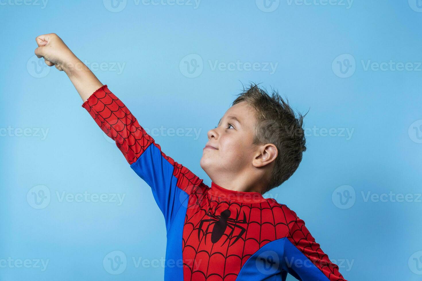 un chico en un héroe traje. un victorioso hacia arriba movimiento de el mano foto