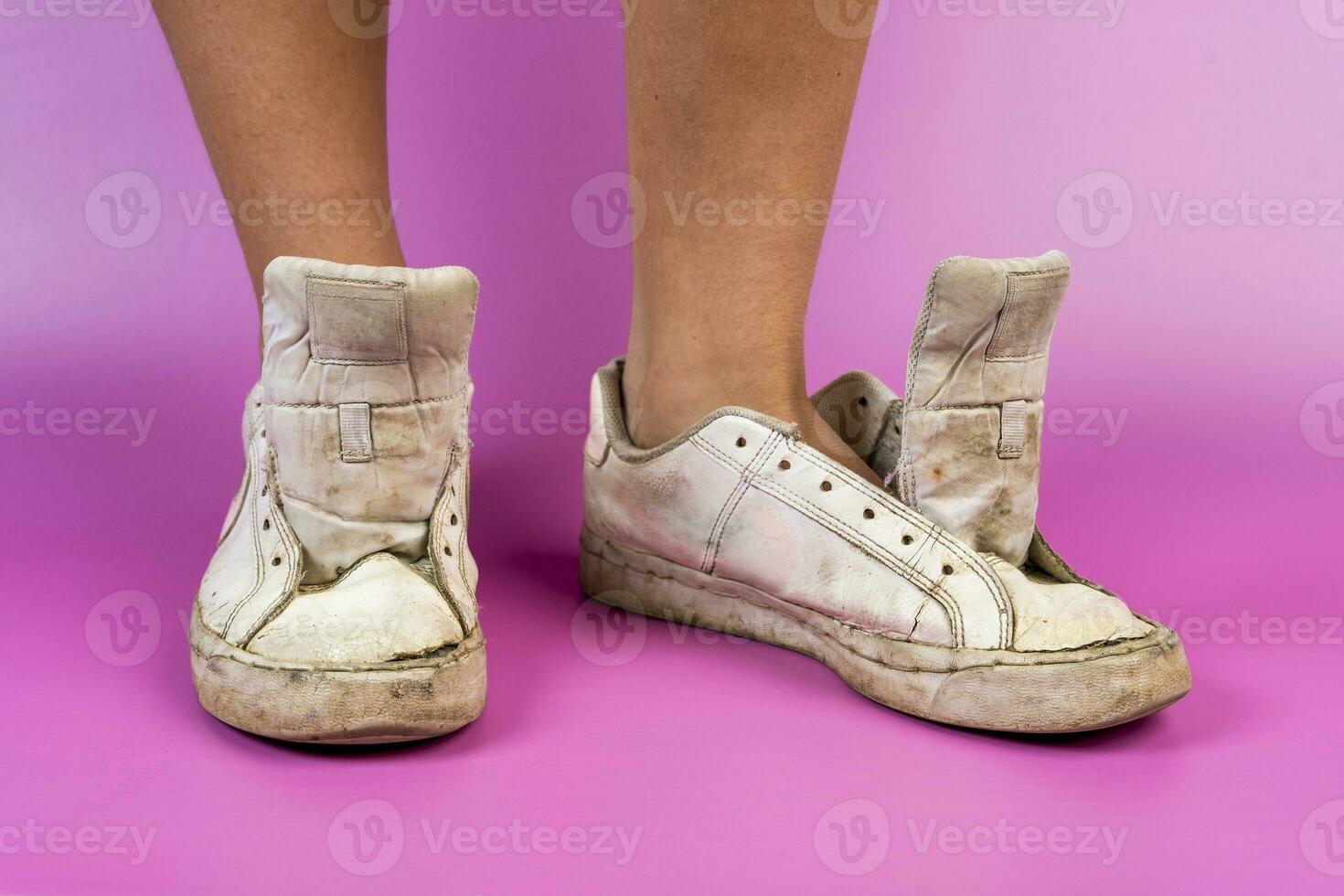 women's legs shod in old battered sneakers on a pink background photo