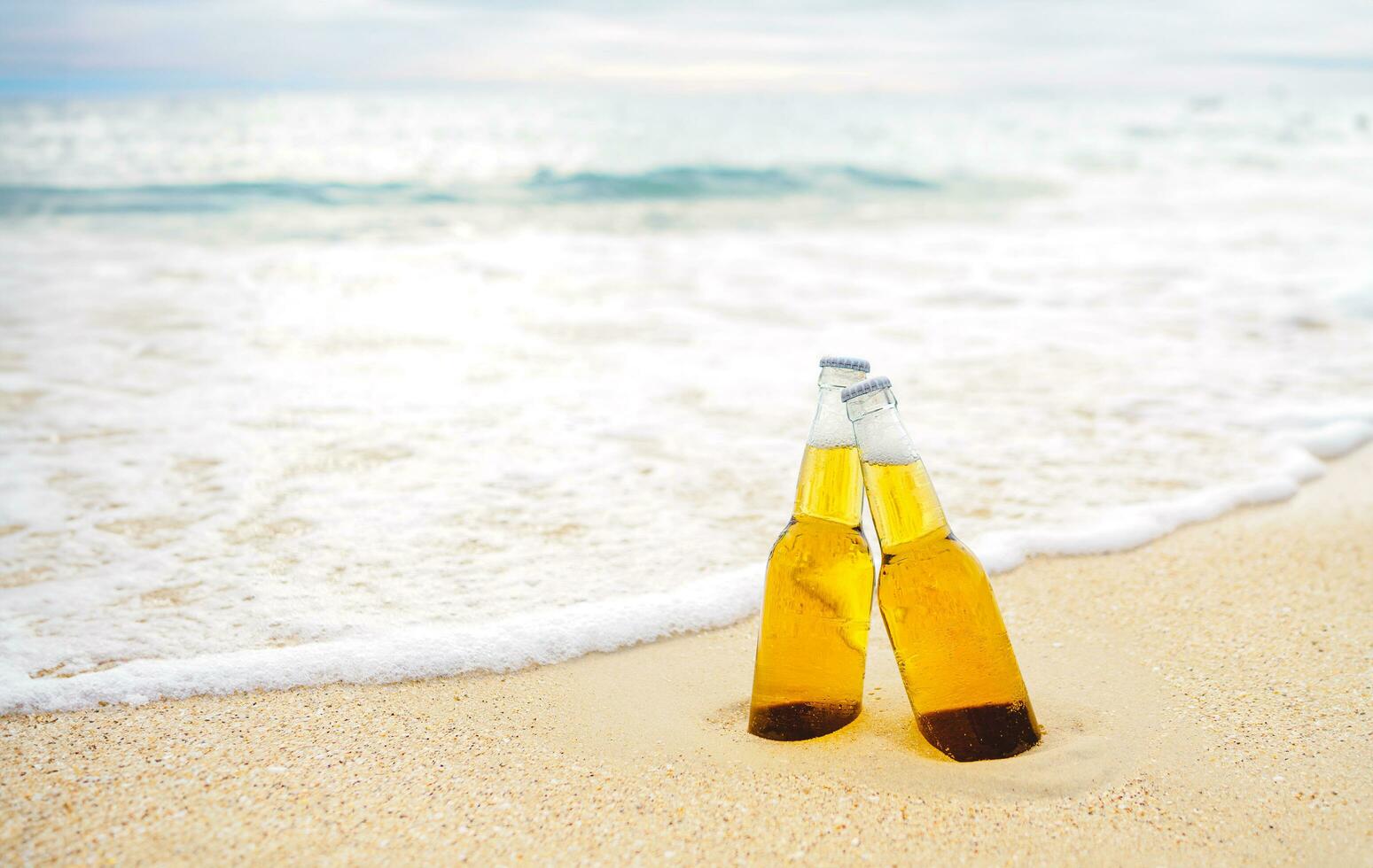 botellas de cerveza en el arenoso playa con mar Oceano antecedentes. fiesta, amistad, cerveza concepto. foto