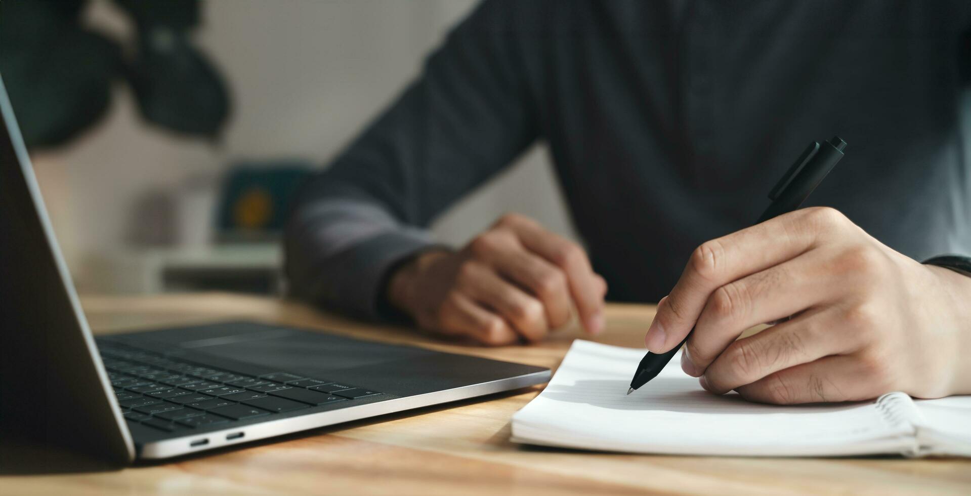 left handed man writes in a notebook on the table with laptop computer, Businessman. photo