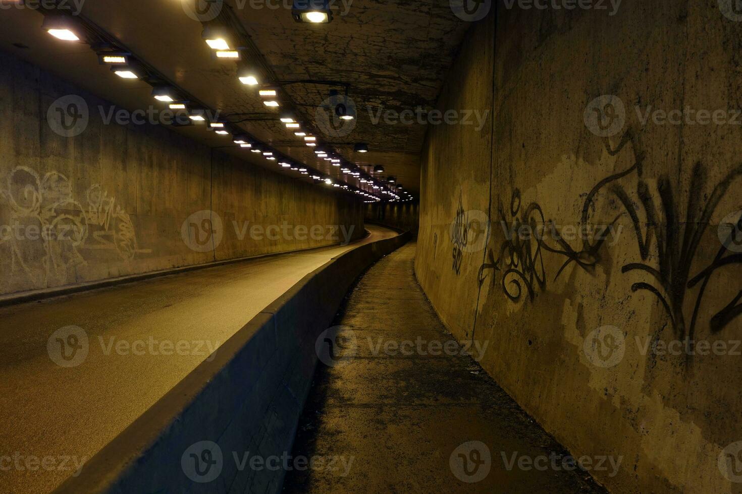 Grimy, dimly lit, empty urban underpass road and sidewalk with graffiti on concrete walls photo