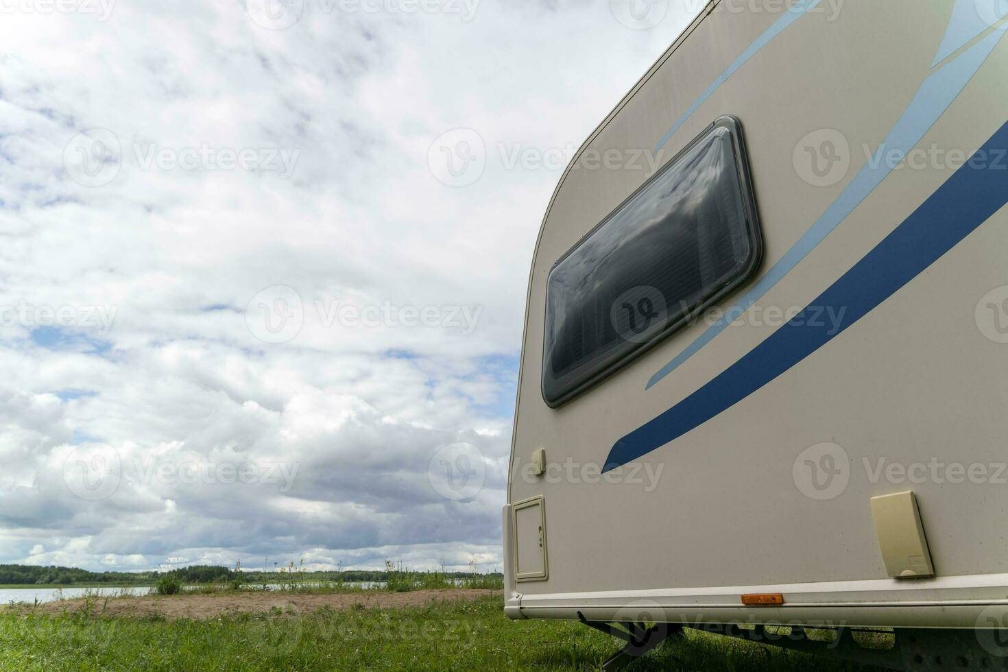 Camper trailer for traveling standing on shore of the lake in summer photo
