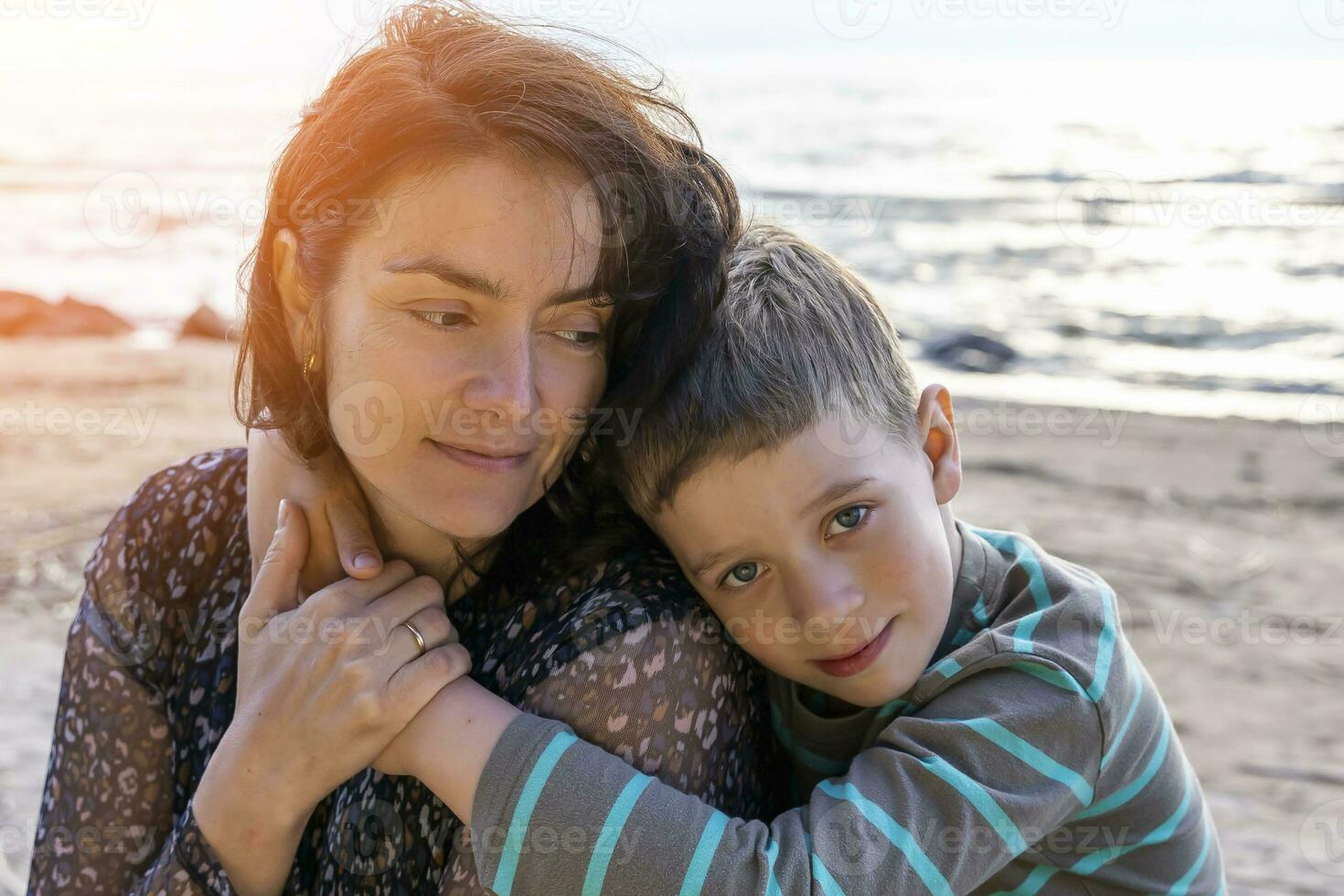 Cute happy boy hugs his mom by the sea. looking into the camera photo