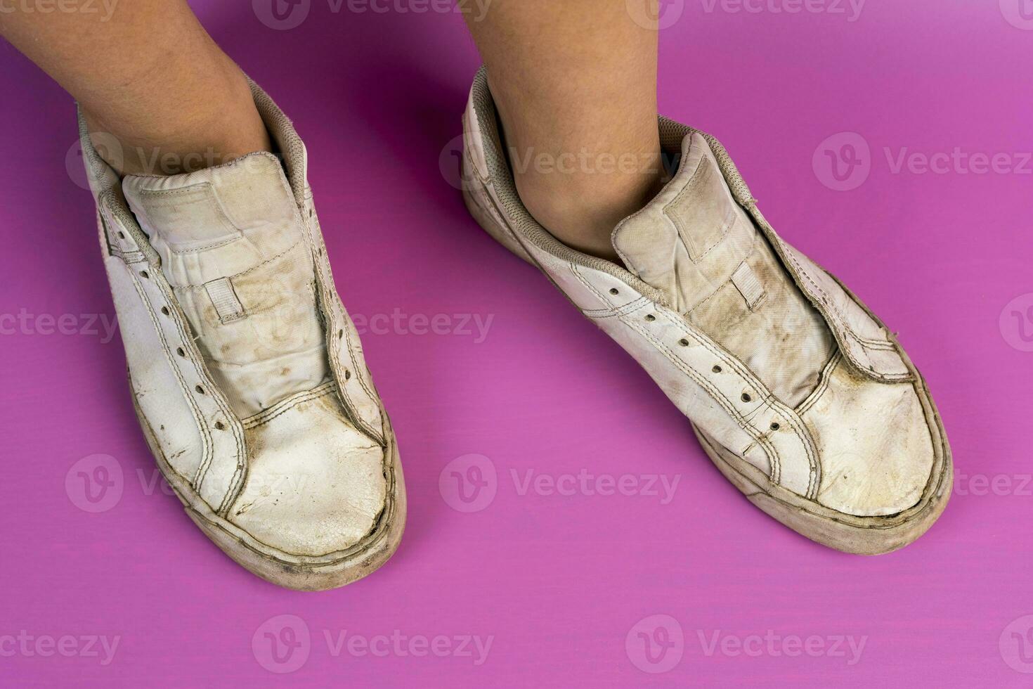 women's legs shod in old battered sneakers on a pink background photo