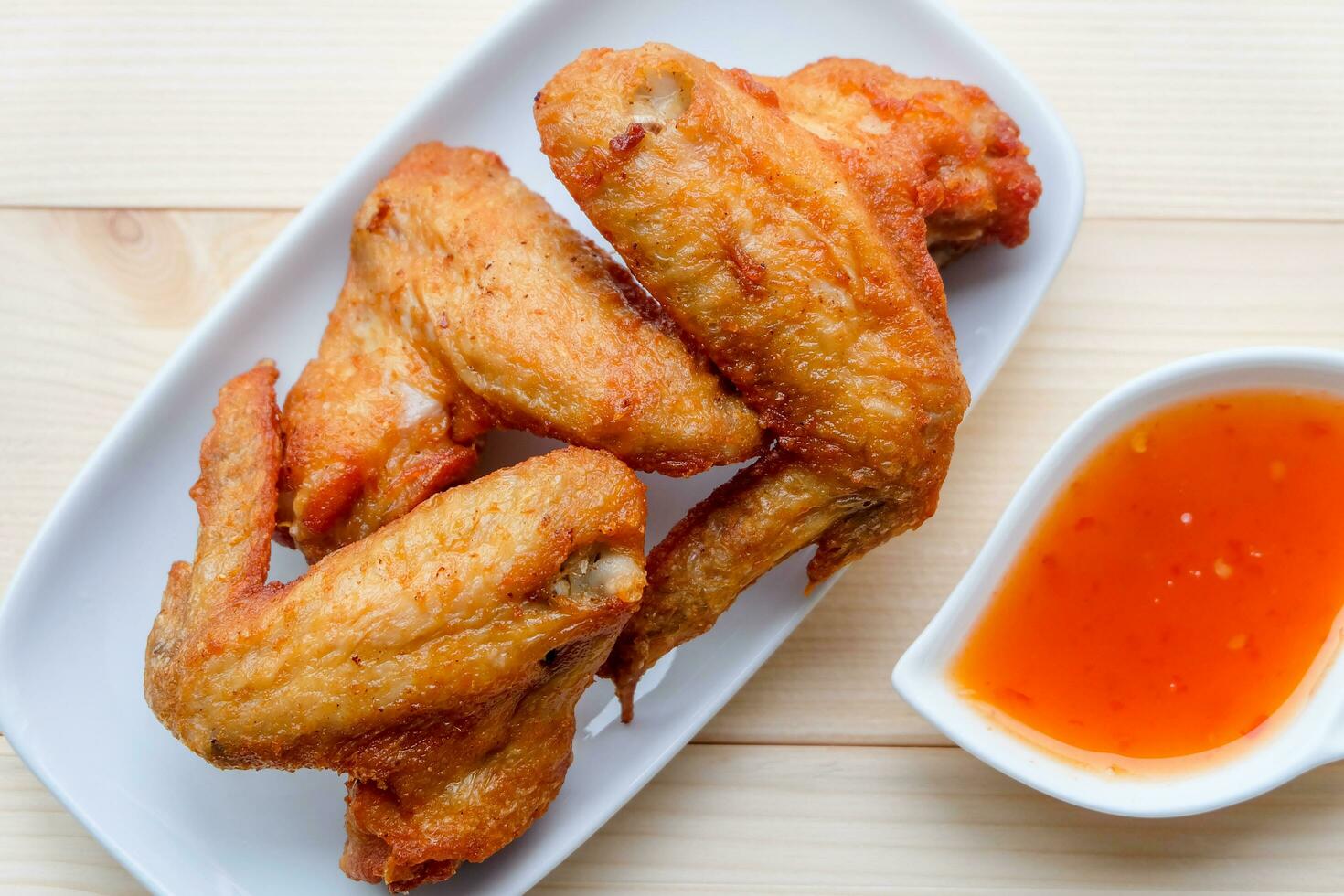 Top view and close up Deep Fried Chicken wing in white plate with sweet sauce on wooden background. Popular food for kids. photo
