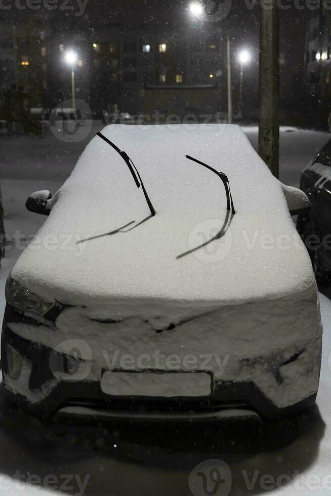Windshield of a car covered with snow and wiper blades raised up photo