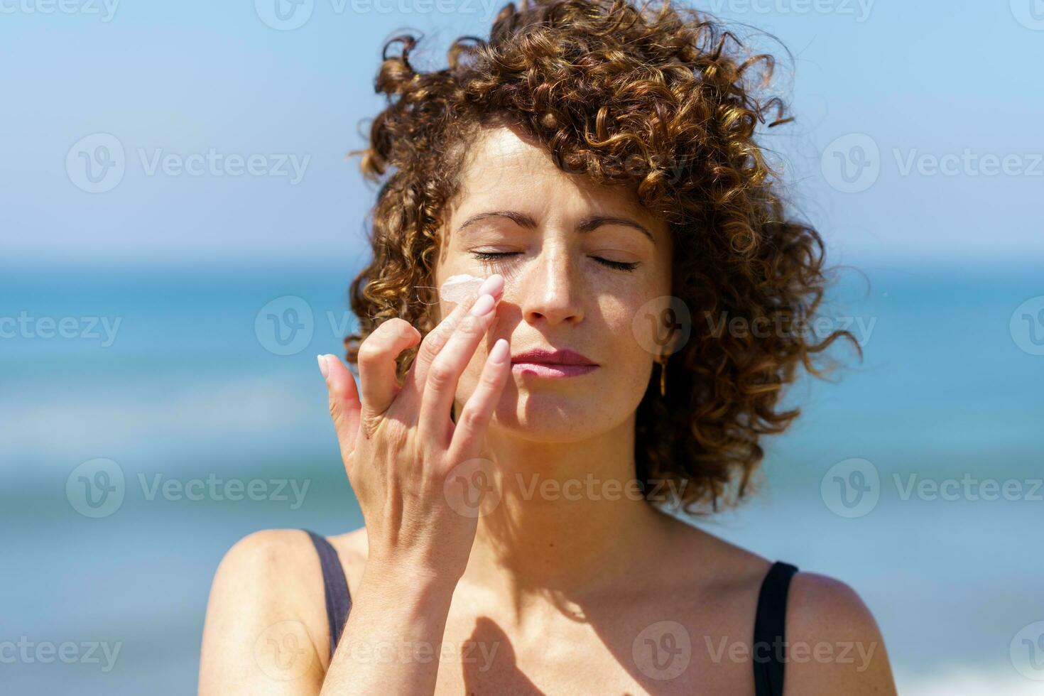Sensual woman applying sunscreen on face photo