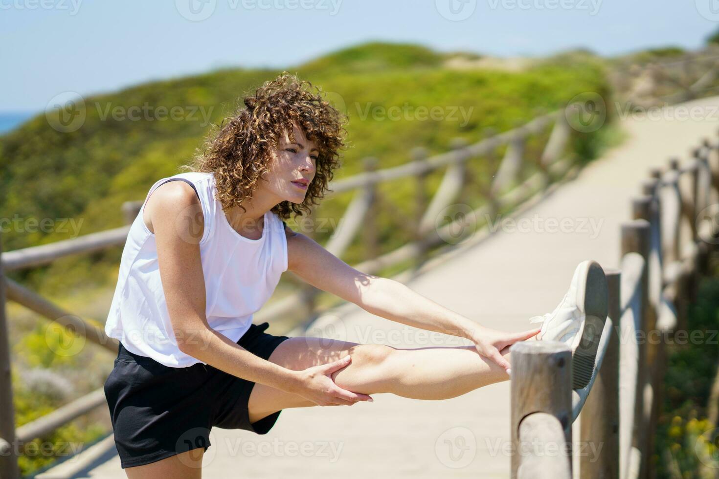 Focused young woman stretching leg on wooden bridge photo