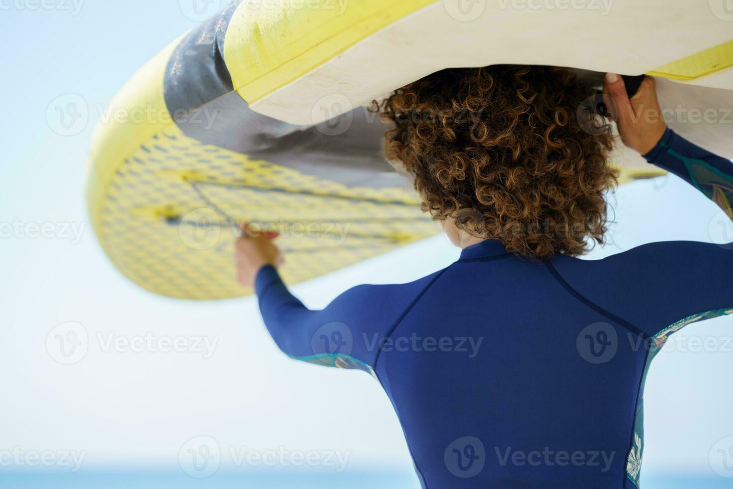 Unrecognizable woman lifting paddleboard over head on shore photo