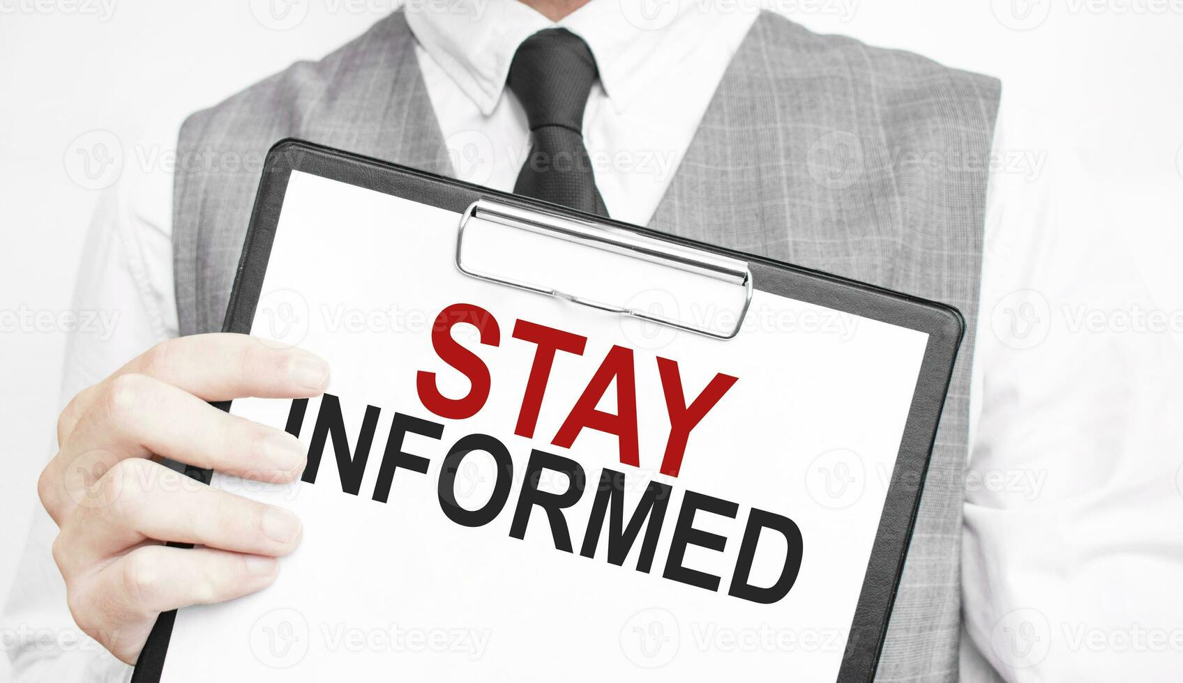STAY INFORMED inscription on a notebook in the hands of a businessman on a grey background, a man points with a finger to the text photo