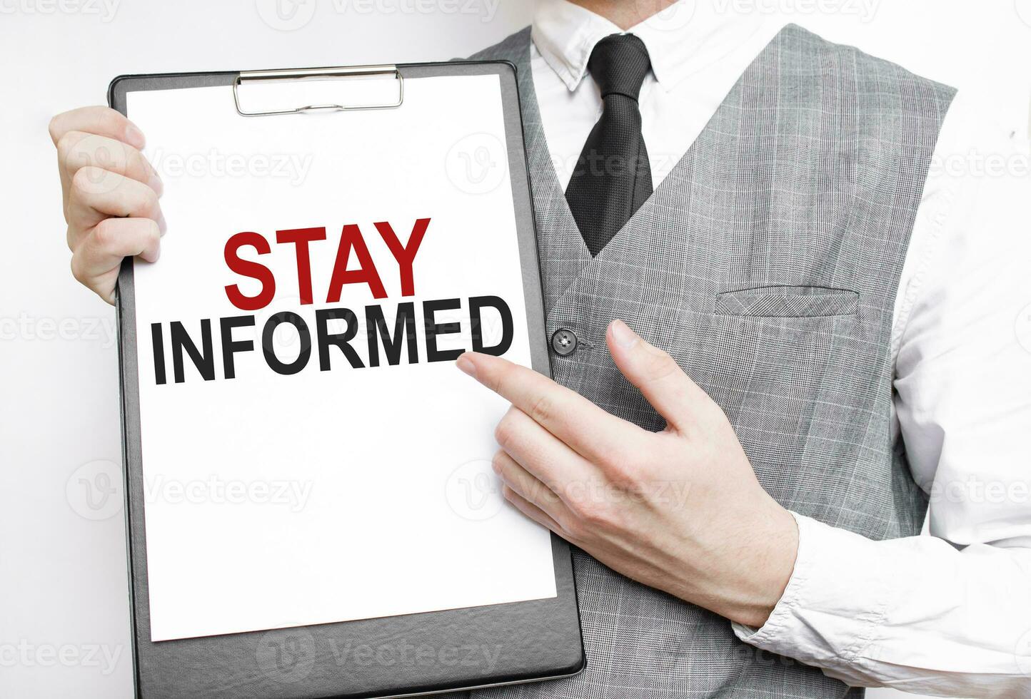 STAY INFORMED inscription on a notebook in the hands of a businessman on a grey background, a man points with a finger to the text photo