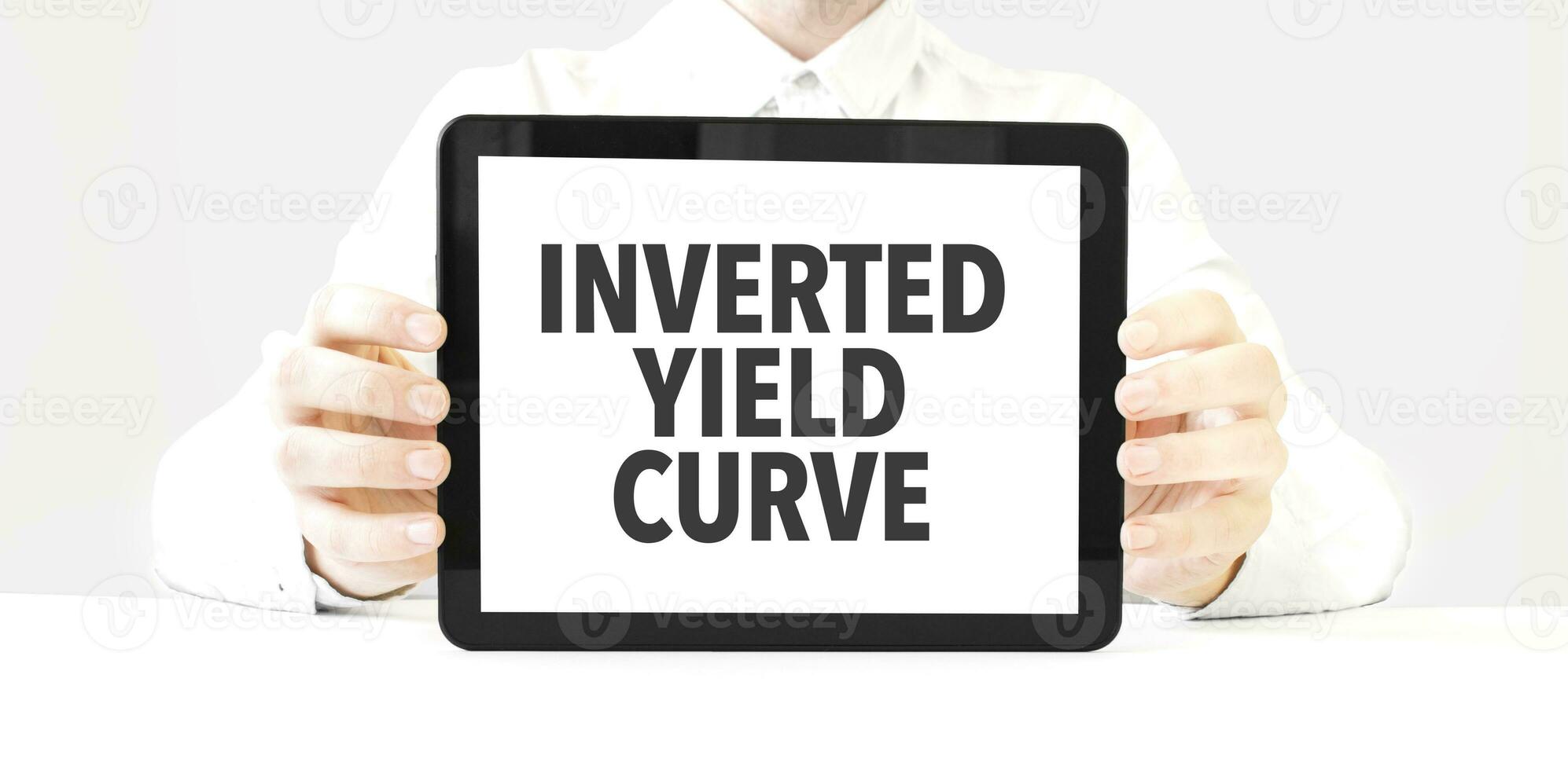 Text INVERTED YIELD CURVE on tablet display in businessman hands on the white background. Business concept photo