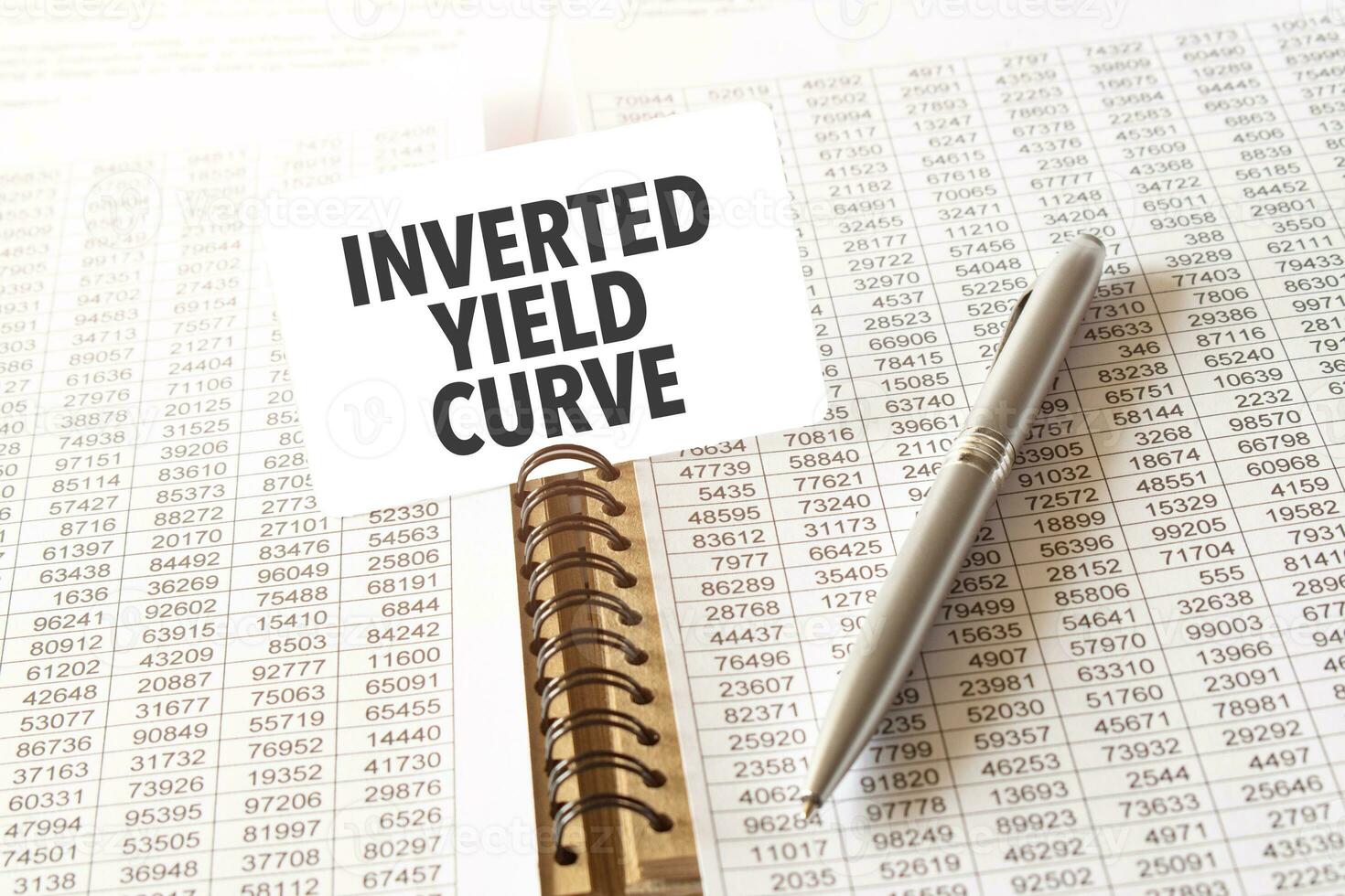 Text INVERTED YIELD CURVE on paper card, pen, financial documentation on table photo