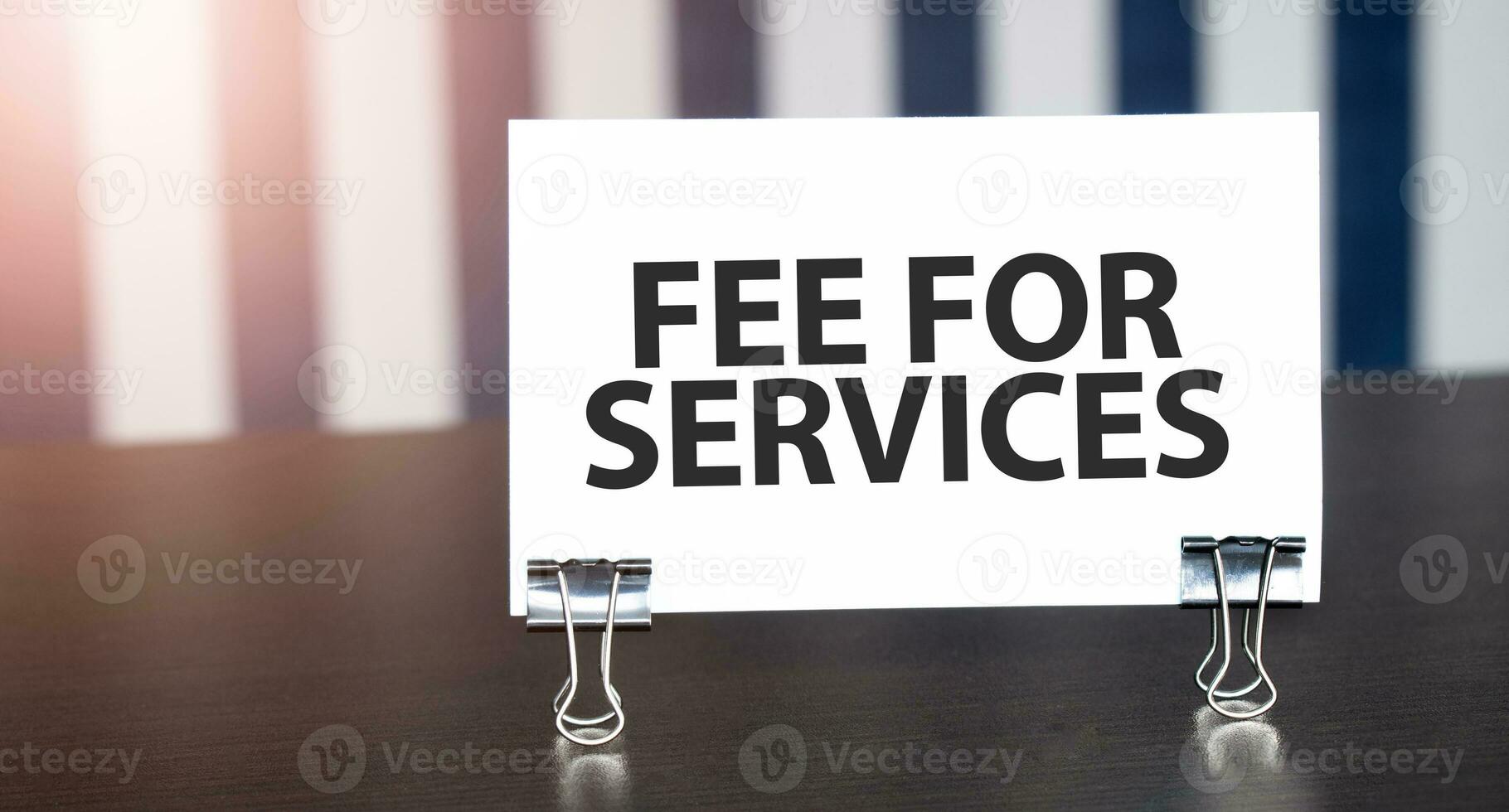 fee for services sign on paper on dark desk in sunlight. Blue and white background photo