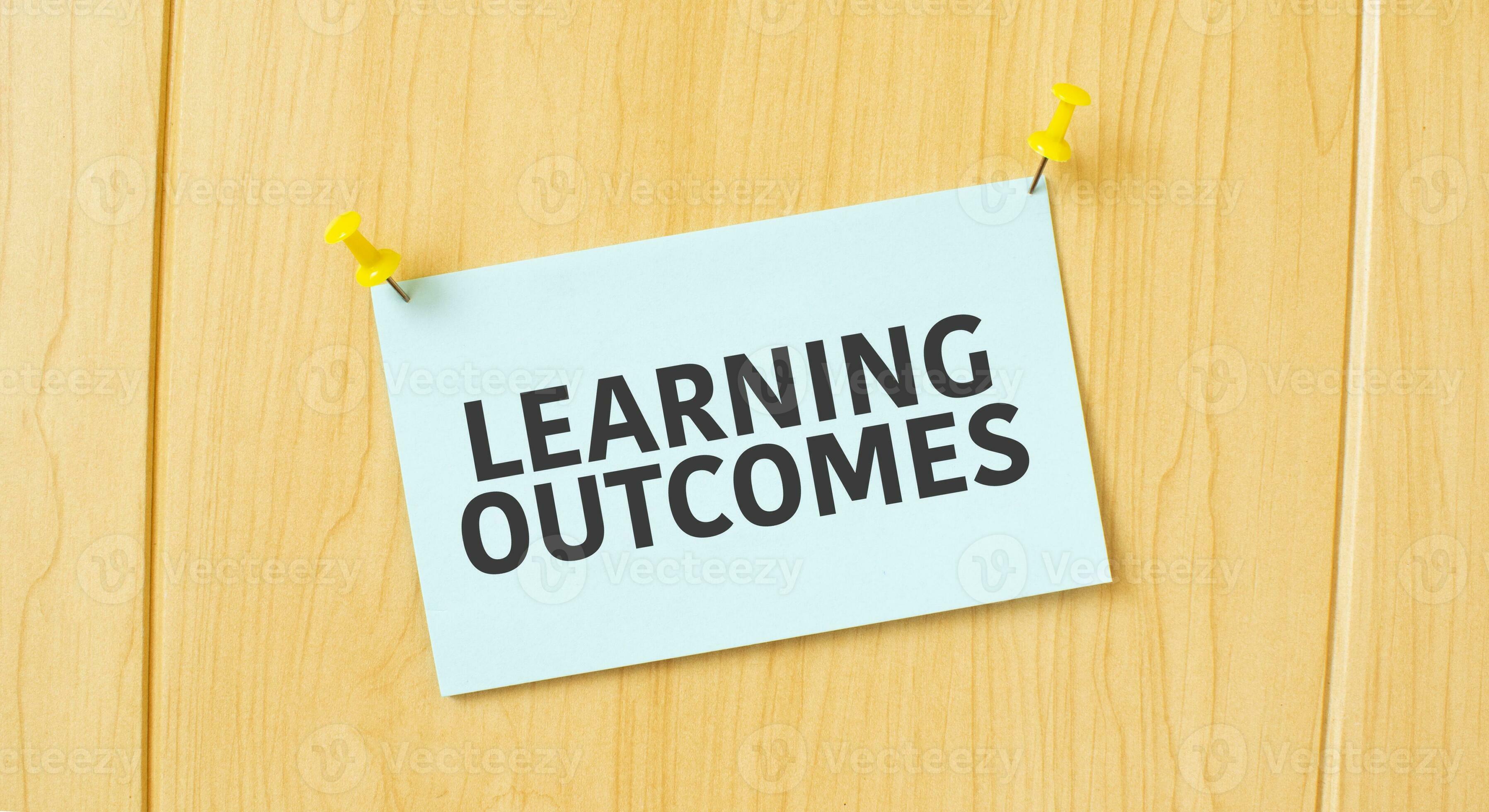 LEARNING OUTCOMES sign written on sticky note pinned on wooden wall ...