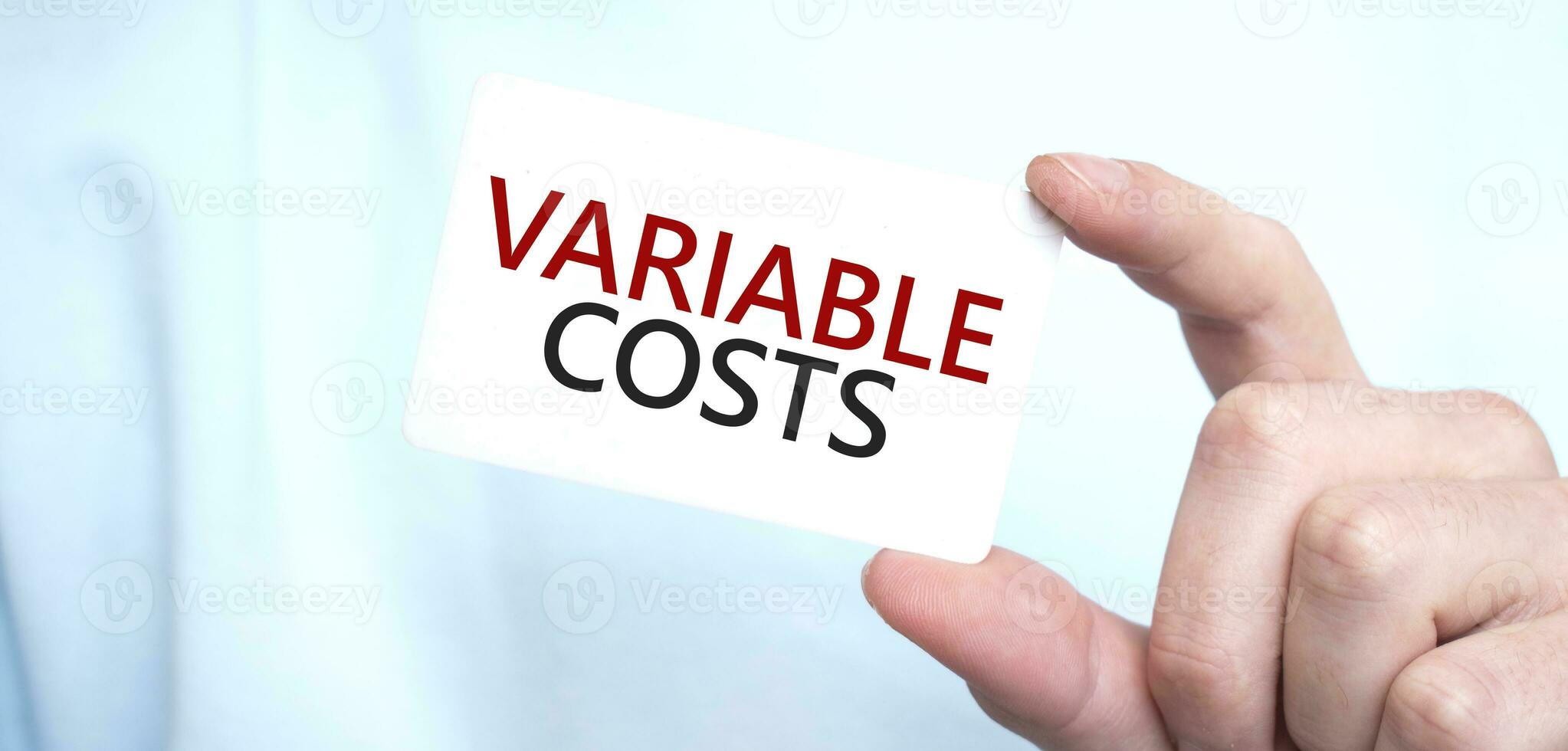 Man in blue sweatshirt holding a card with text VARIABLE COSTS, business concept photo