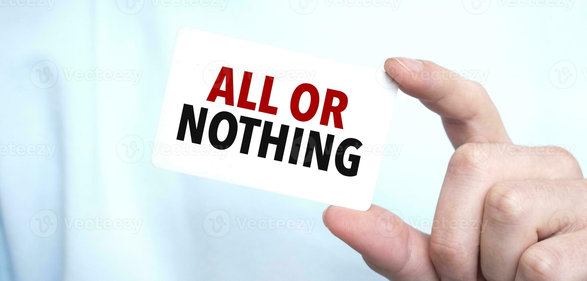 Man in blue sweatshirt holding a card with text ALL OR NOTHING, business concept photo