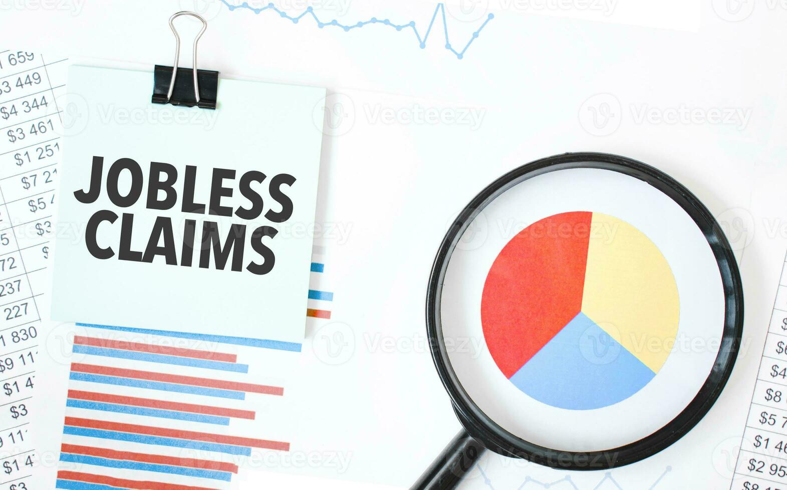 Green card on the white notepad and magnifier on the financial documentation. Text JOBLESS CLAIMS. Business concept photo