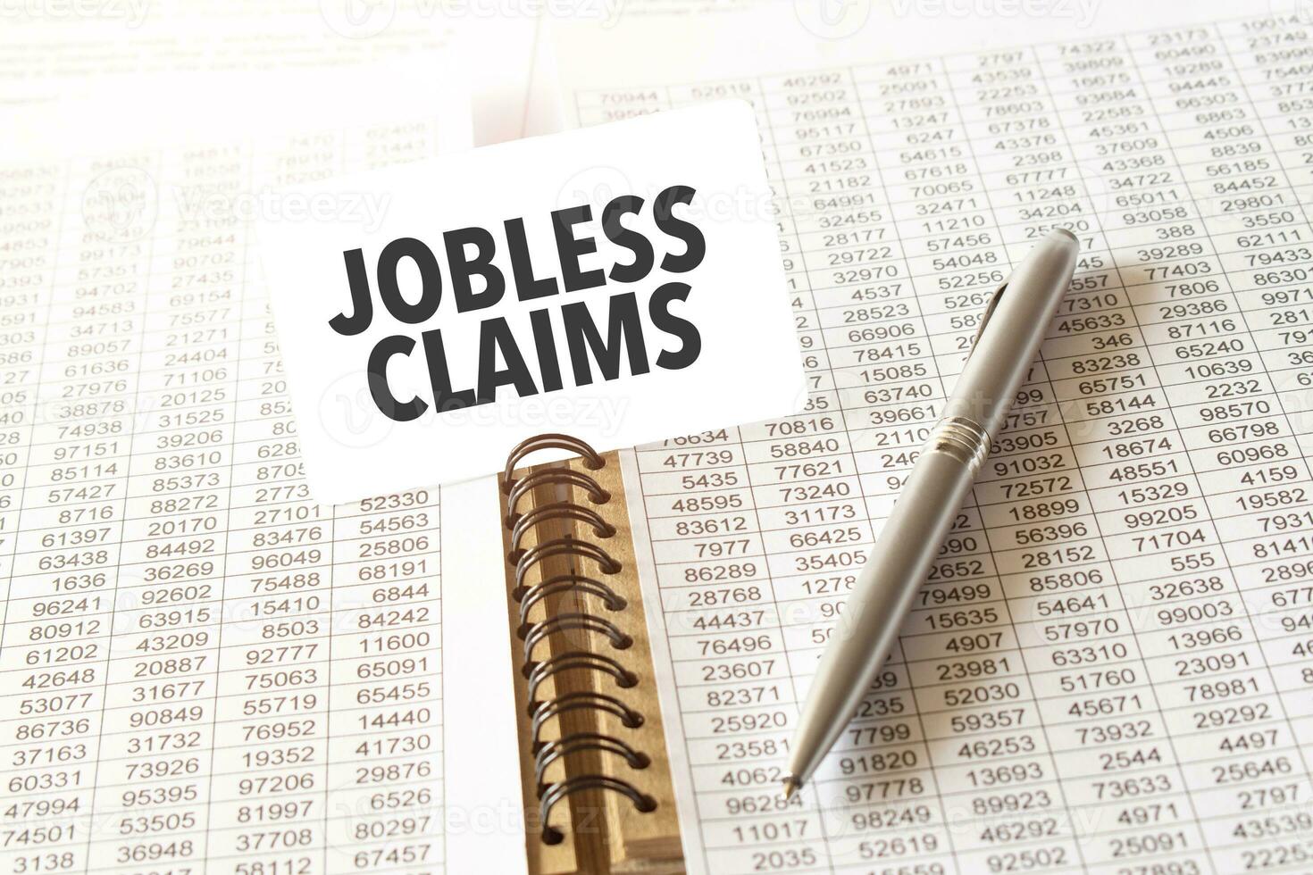 Text JOBLESS CLAIMS on paper card, pen, financial documentation on table photo