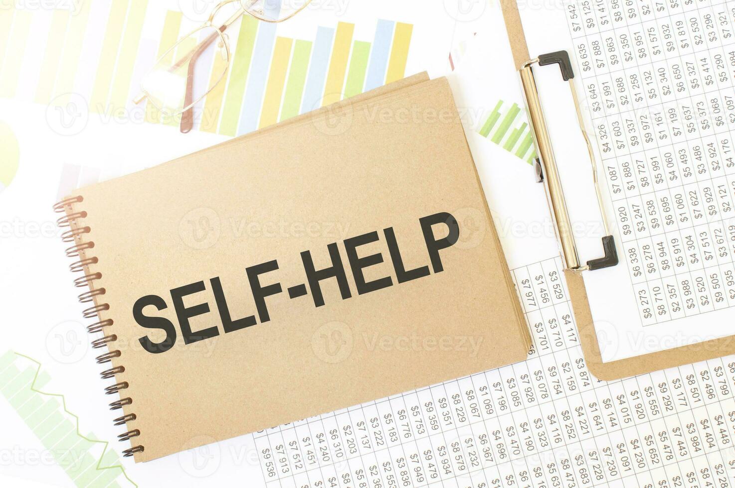 Business up graph on a sheet of craft colour Notepad with SELF HELP sign. Notepad on desk with financial documentation photo