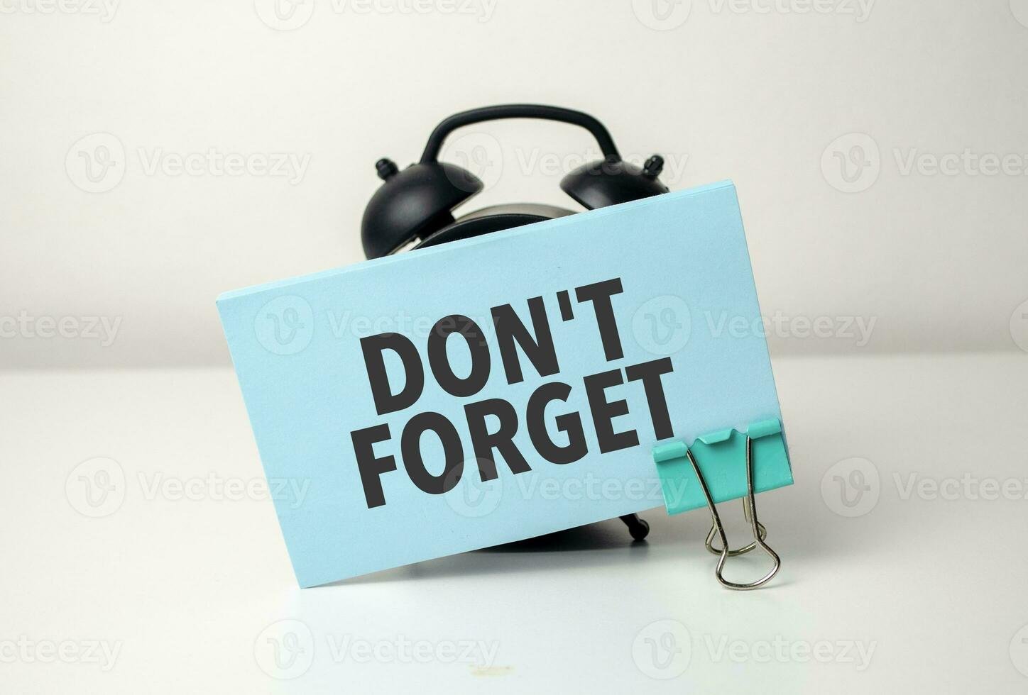 Don't forget is written in a blue sticker near a black alarm clock photo