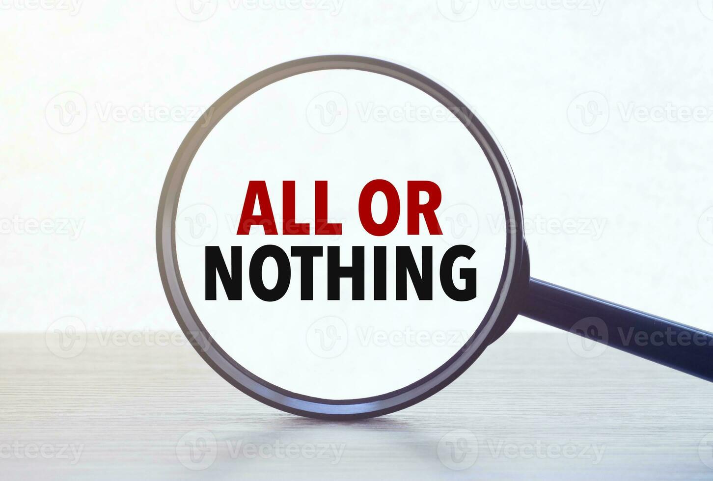 Magnifying glass with text ALL OR NOTHING on wooden table. photo