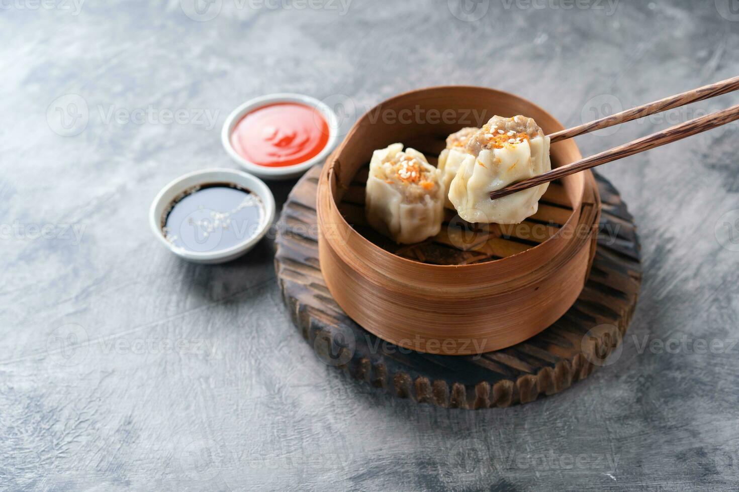 Chinese steamed dumplings or  Dim Sum with chopstick in bamboo steamer on dark abstract background photo