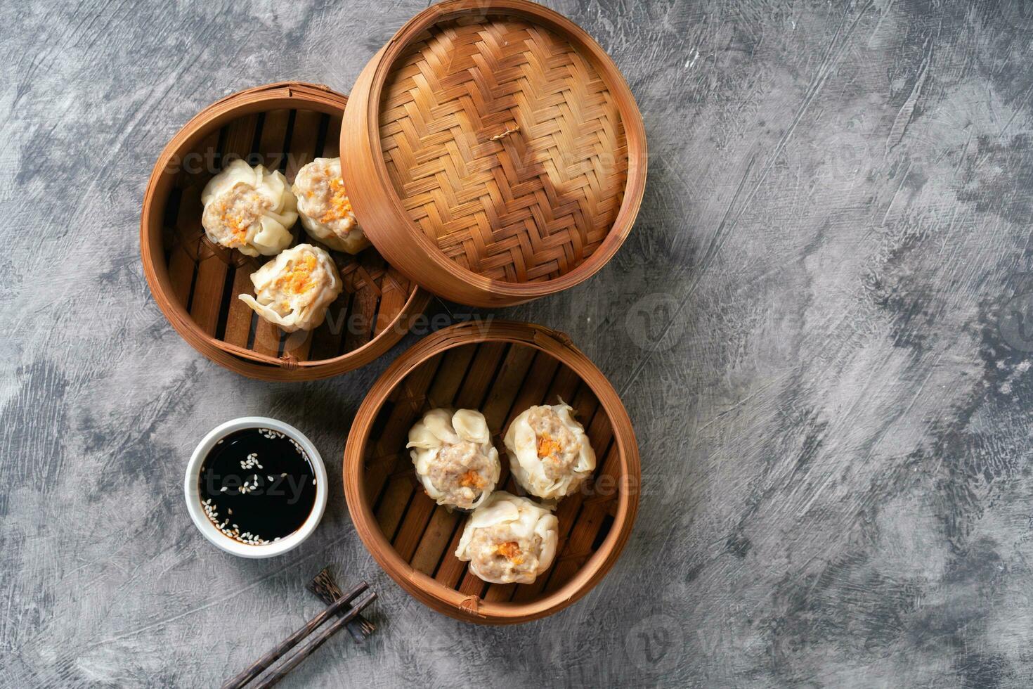 Chinese steamed dumplings or  Dim Sum with chopstick in bamboo steamer on dark abstract background photo