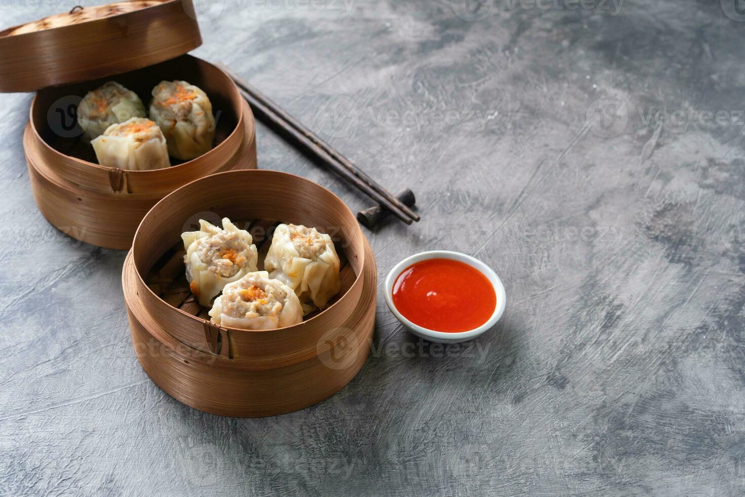 Chinese steamed dumplings or  Dim Sum with chopstick in bamboo steamer on dark abstract background photo