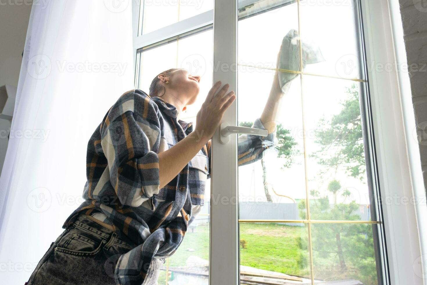 mujer a mano lavados el ventana de el casa con un trapo con rociar limpiador y fregona dentro el interior con blanco cortinas restaurar orden y limpieza en el primavera, limpieza servise foto