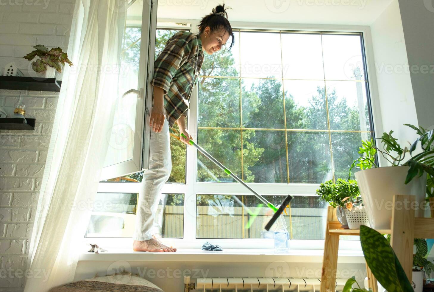 Woman manually washes the window of the house with a rag with spray cleaner and mop inside the interior with white curtains. Restoring order and cleanliness in the spring, cleaning servise photo