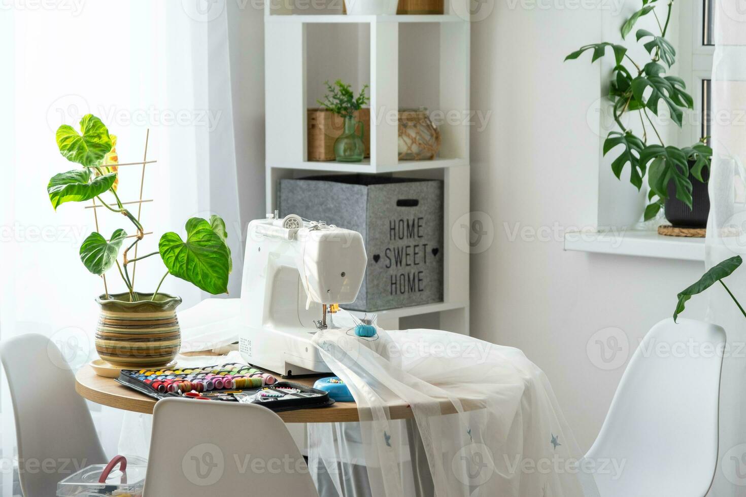 Sewing machine on a round table in the white interior of the house near the window with a transparent curtain, and a home plant in a pot - a modern interior. hobby, home business photo