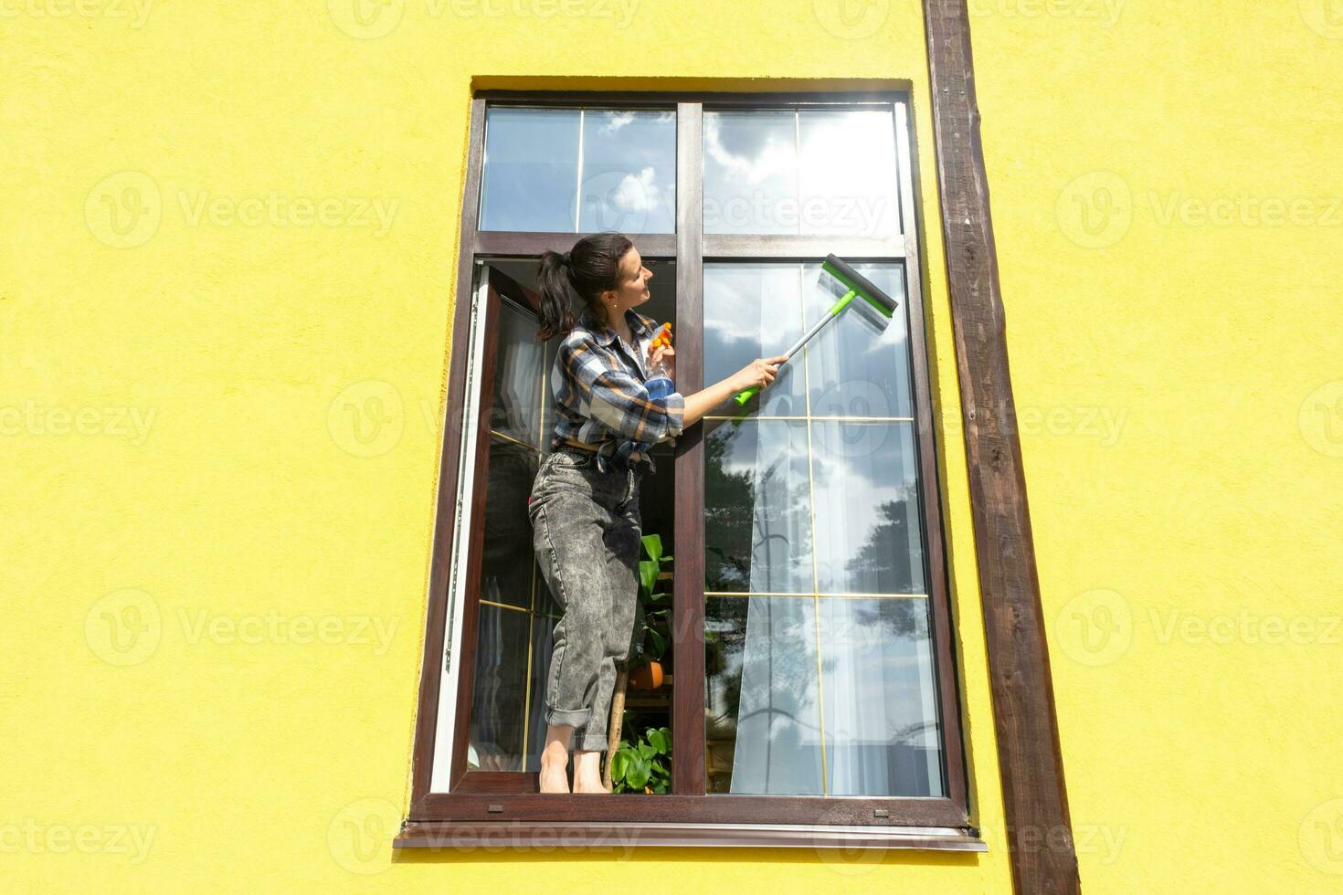 un mujer a mano lavados el ventana de el casa con un trapo con un rociar limpiador y un fregona afuera. la seguridad a altura, restaurar orden y limpieza en el primavera, limpieza Servicio foto