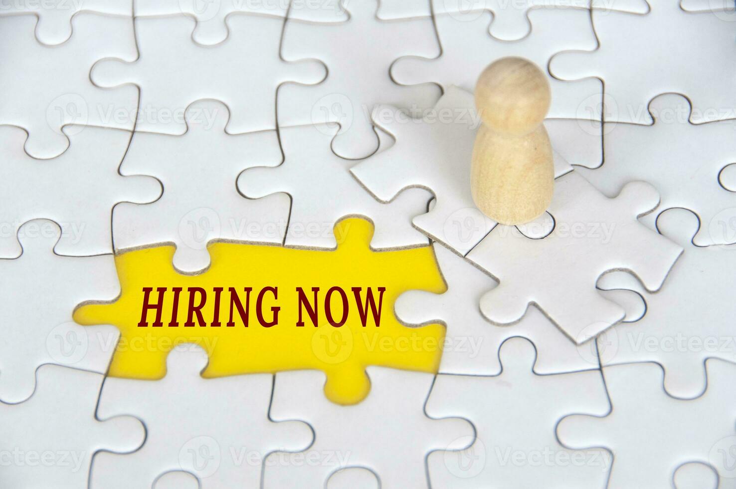 Hiring now text on missing jigsaw puzzle with wooden figure background. Employment concept photo