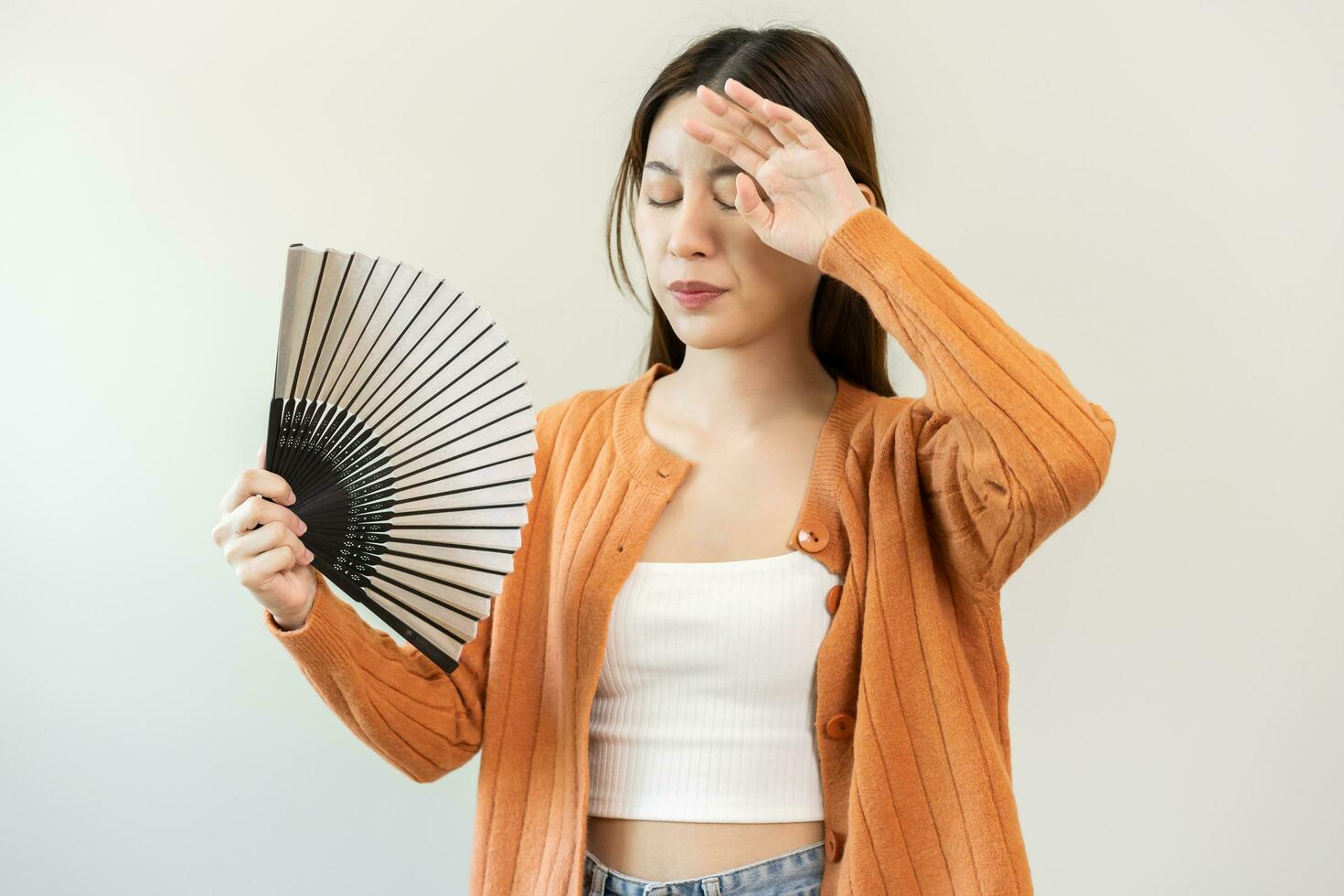 Suffering summer heat stroke, hot weather, tired asian young woman, girl sweaty and thirsty, refreshing with hand in blowing, wave fan to ventilation when temperature high at home, house on background photo