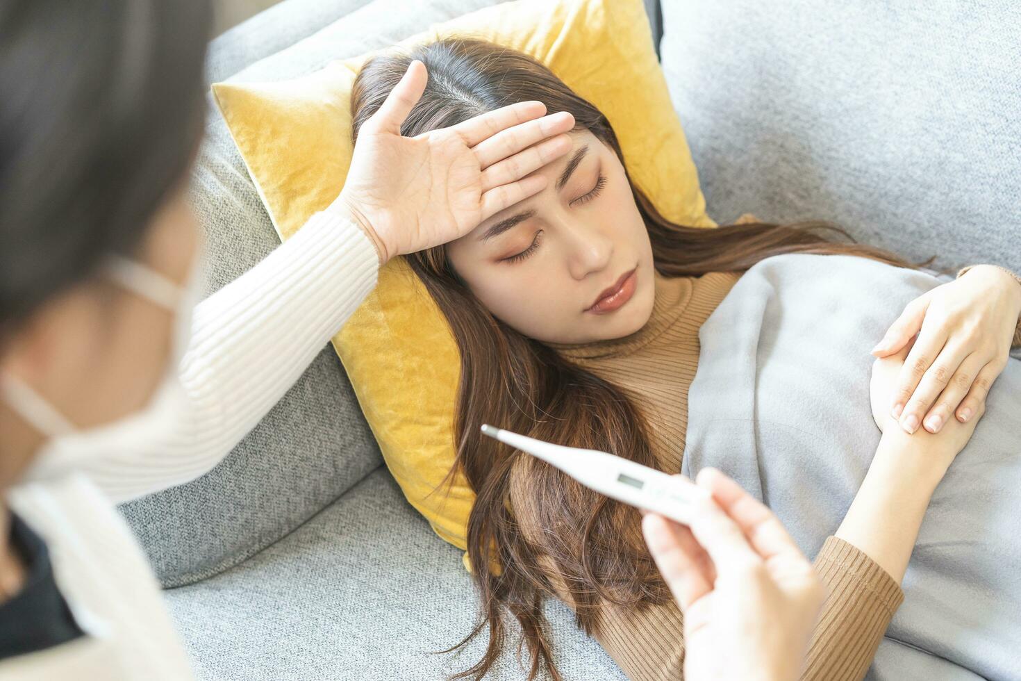Sick, influenza asian young woman, girl headache have high fever, flu check thermometer measure body temperature, feel illness while lying on sofa, couch at home. Health care, infection of covid-19. photo