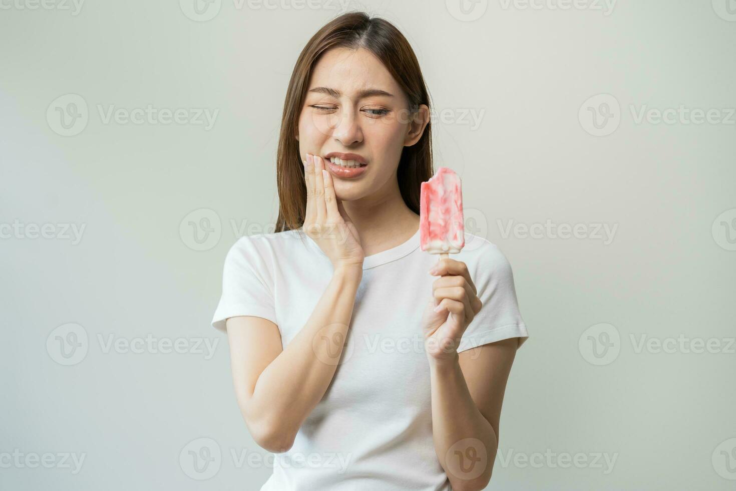 Face expression suffering from sensitive teeth and cold, asian young woman, girl feeling hurt, pain eating ice cream, lolly. Toothache molar tooth at home, dental problem isolated on white background. photo