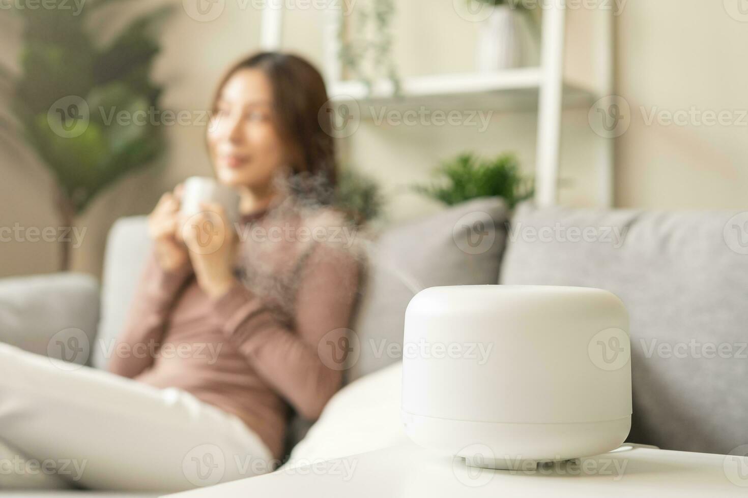 Modern air humidifier during relax or rest, happy blurred asian young woman, girl enjoying aromatherapy steam scent from essential oil diffuser comfortable in living conditions room,apartment at home photo