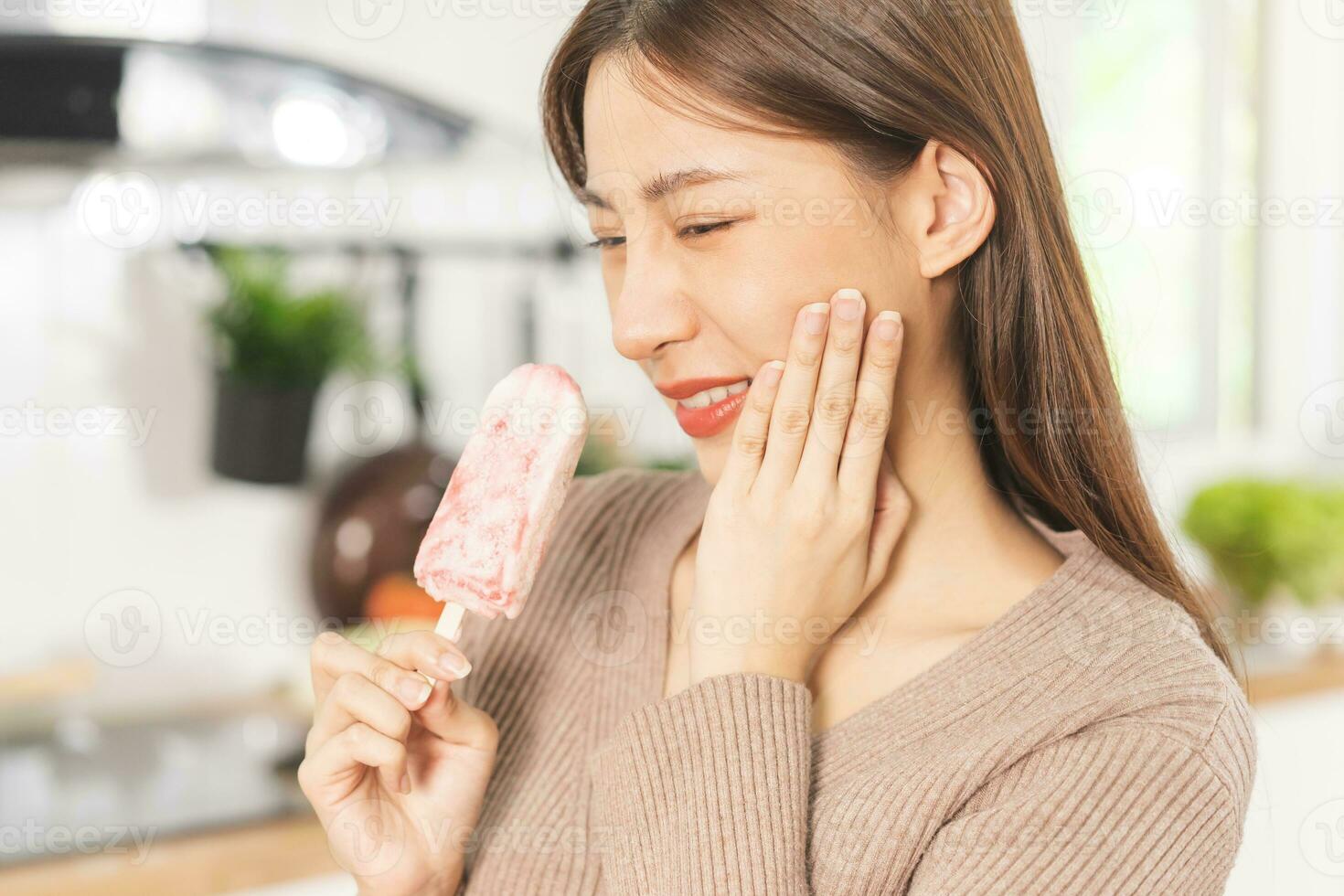 Face expression suffering from sensitive teeth and cold, asian young woman, girl hand touching her cheek, feeling hurt, pain eating ice cream, lolly. Toothache molar tooth at home, dental problem. photo