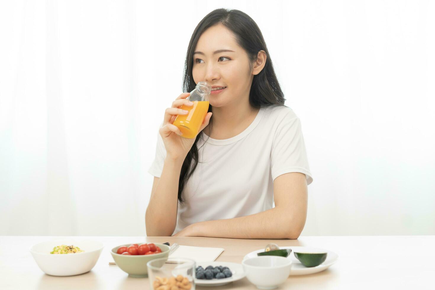Happy smile asian young woman, girl drinking fresh orange juice in a glass bottle, holding transparent glass in hand, thirsty at home. Healthcare, healthy diet concept, isolated on white background. photo