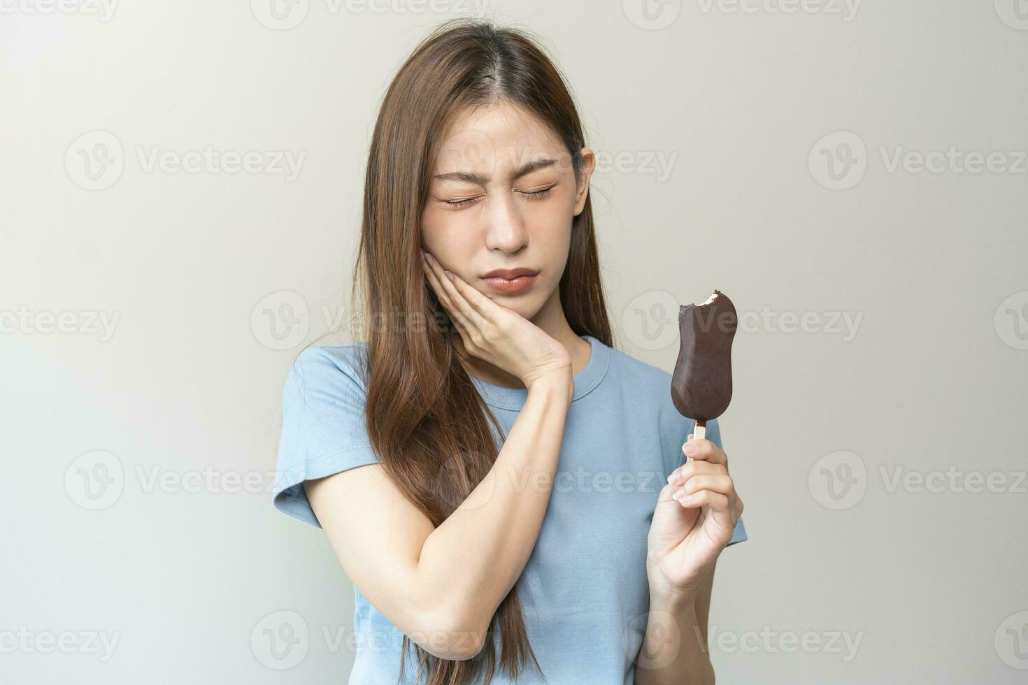 Face expression suffering from sensitive teeth and cold, asian young woman, girl hand touching her cheek, feeling hurt, pain eating ice cream, lolly. Toothache molar tooth at home, dental problem. photo