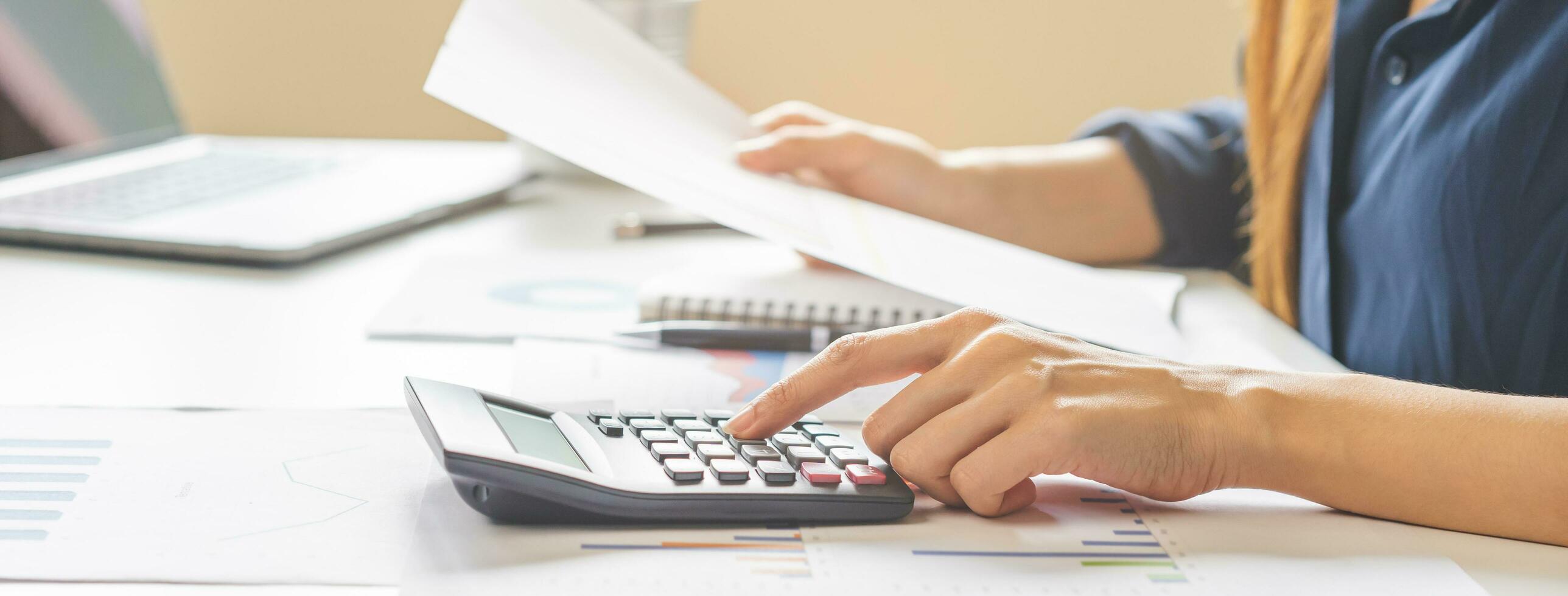 Account finance, asian young business woman hand use calculator for calculate budget, cost and income of company from charts, reports paperwork, plan spend money expenses, working on desk at home. photo