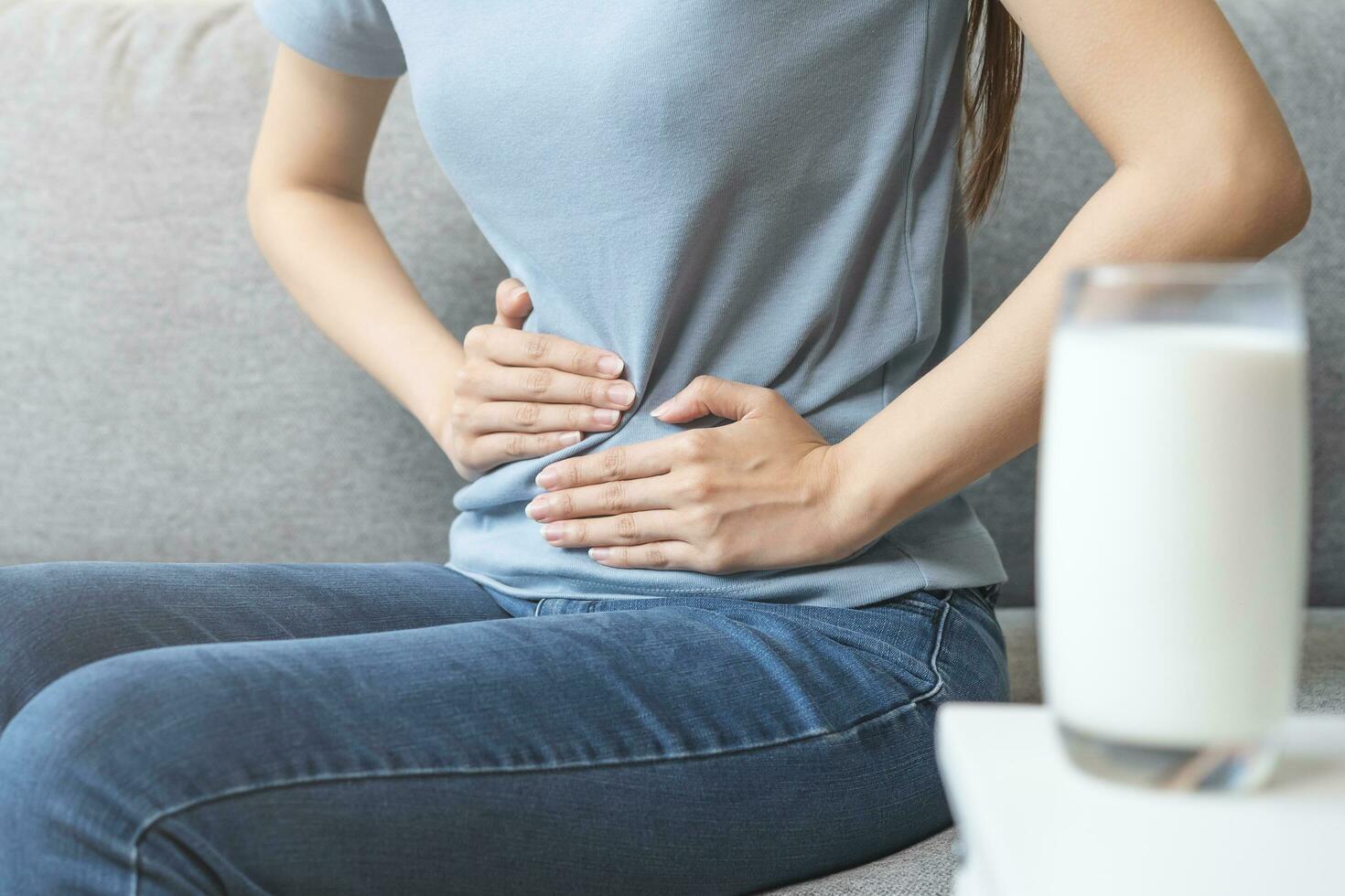 Pain, suffering asian young woman having a stomachache, abdominal pain or digestive, hand in holding belly after drink glass of milk. Lactose intolerance, allergy from dairy food, health care problem. photo