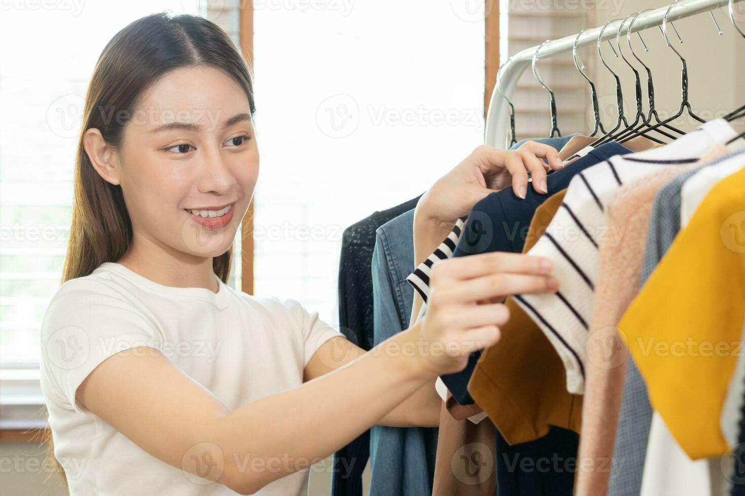 Choice of clothes,Nothing to wear. Attractive asian young woman, girl try on appare, happy choosing dress, outfit on hanger in wardrobe in room closet at home. Deciding blouse what to put on which one photo