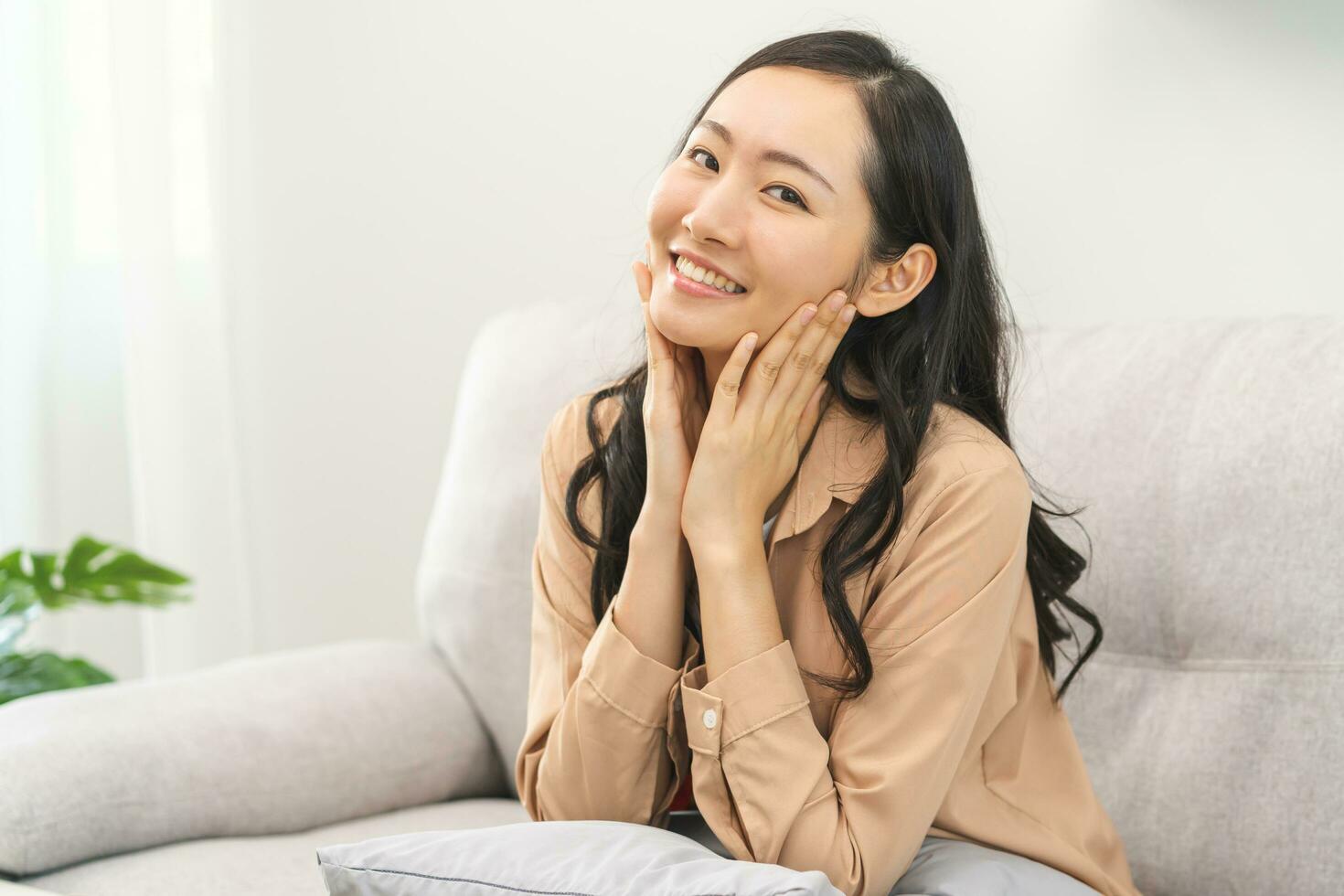 Smiling positive, attractive asian young woman in casual dress, pretty girl sitting on cozy sofa, couch rest, relax at home, portrait of beautiful with long black hair, feeling happy looking at camera photo