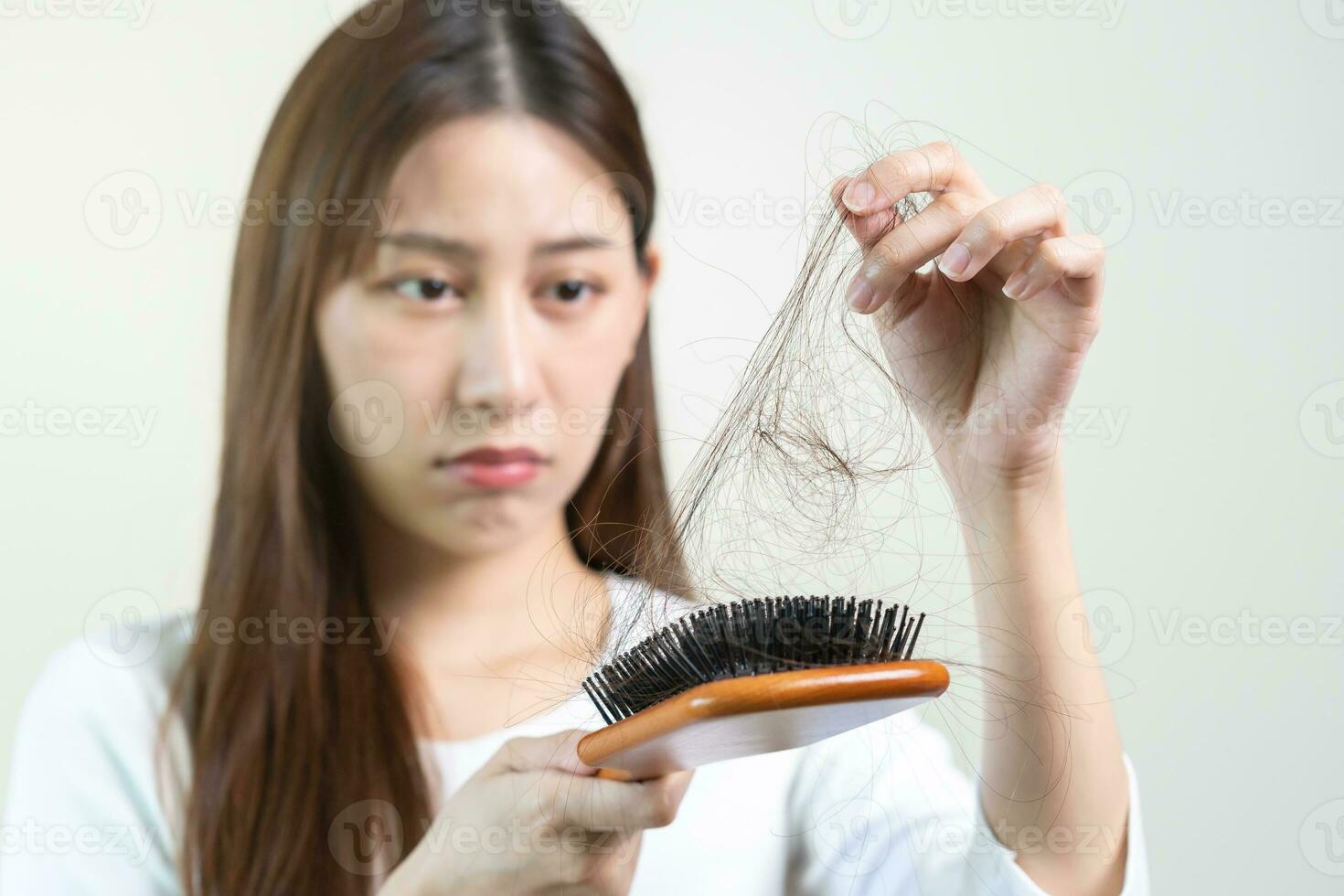 Serious, worried asian young woman, girl holding brush, show her comb, hairbrush with long loss hair problem after brushing, hair fall out on her hand in living room. Health care, beauty treatment. photo